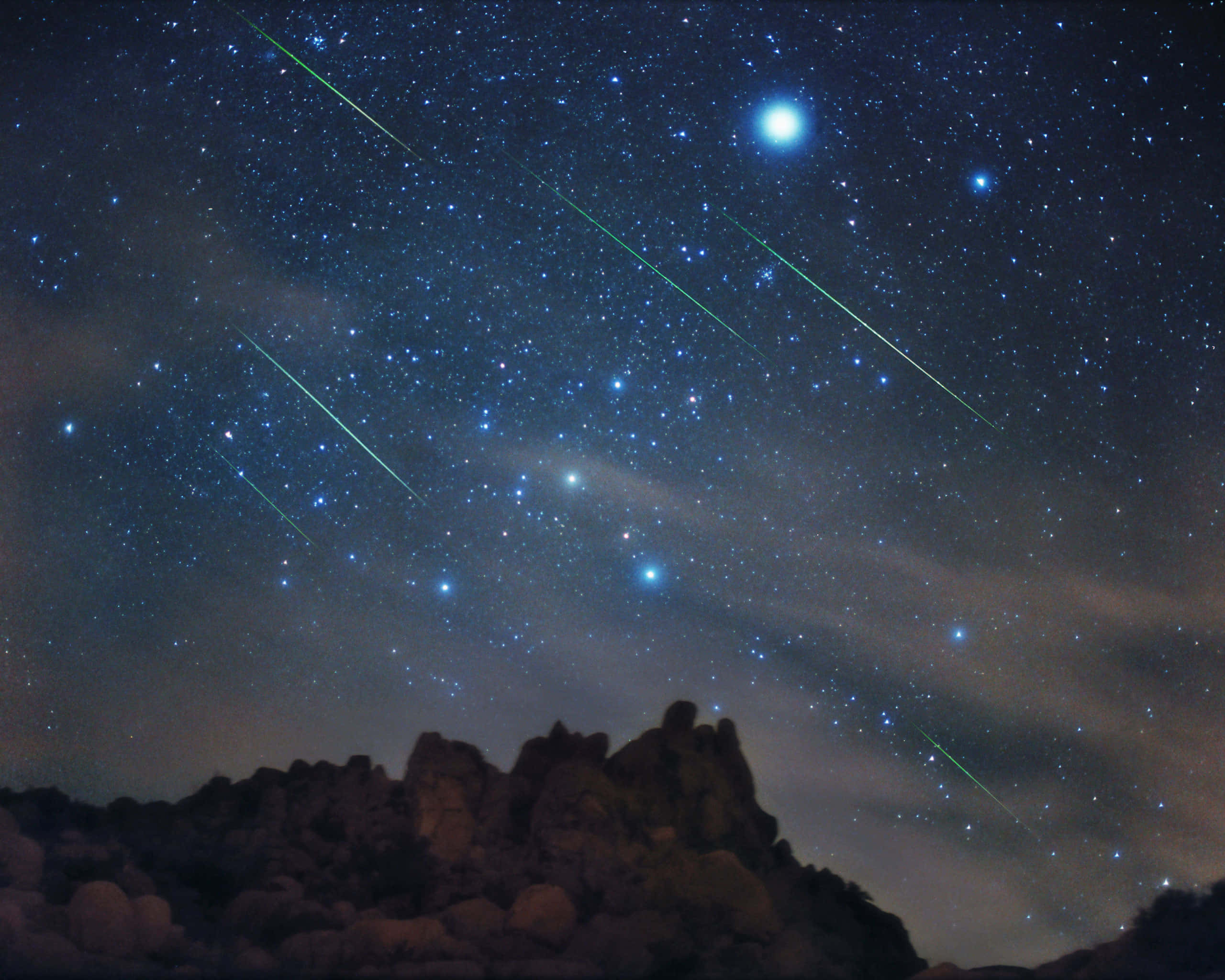 meteor 桌布 壁紙 — 星光燦爛的夜空，明亮的流星在崎嶇岩石地形上劃過，下方是一輪明亮的月亮。