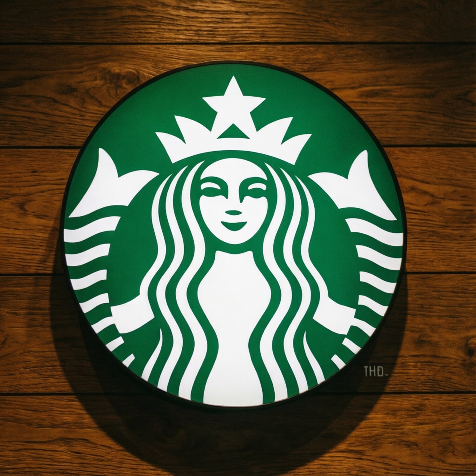 星巴克木紋美人魚 壁紙 — 一個發光的綠色Starbucks海妖標誌安裝在溫暖的木牆板上。