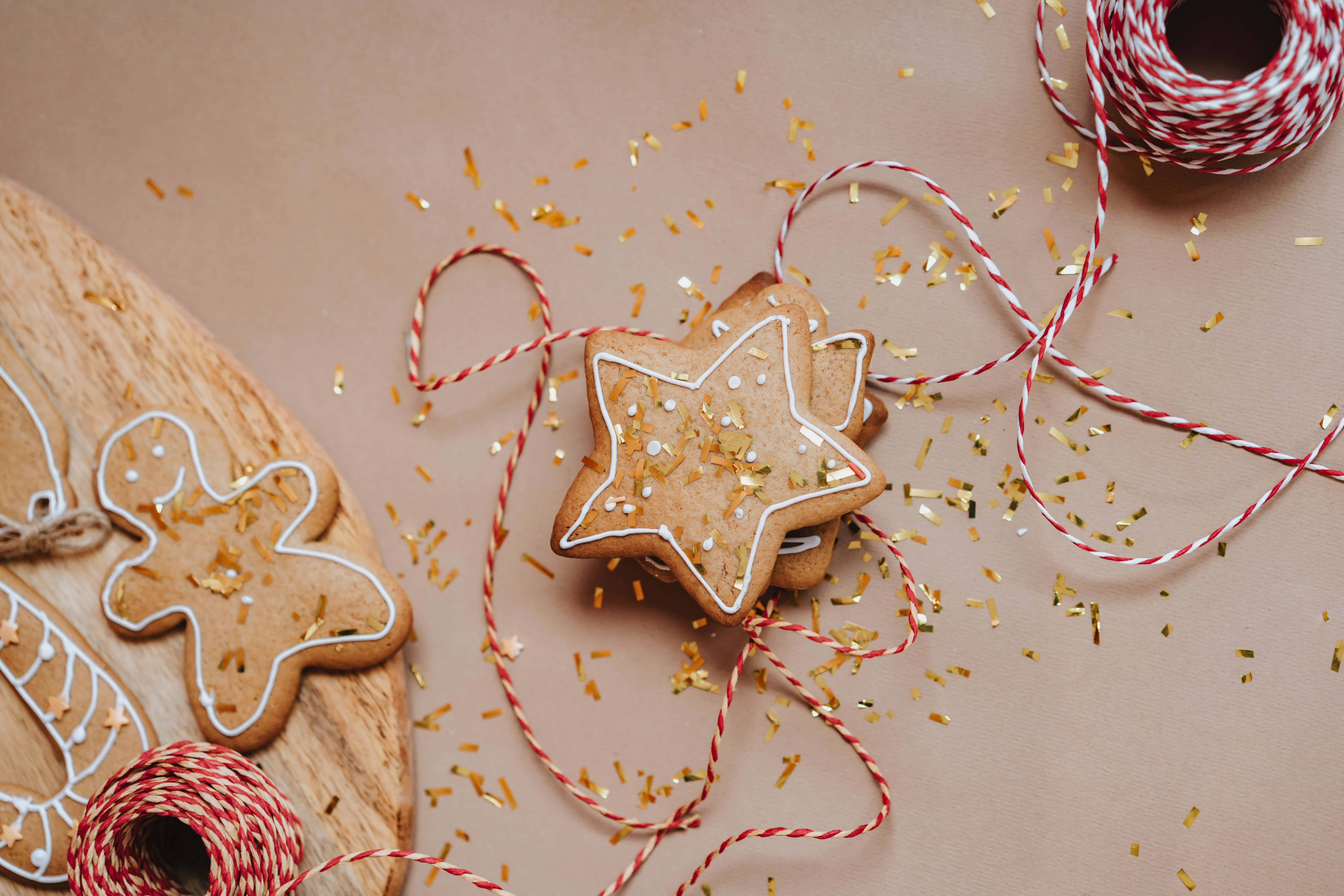 Christmas Star 桌布 壁紙 — 星形和男人形狀的薑餅餅乾，飾以白色糖霜和金糖粒，放在木板上，配有紅白繩子和散落的金色五彩紙屑。