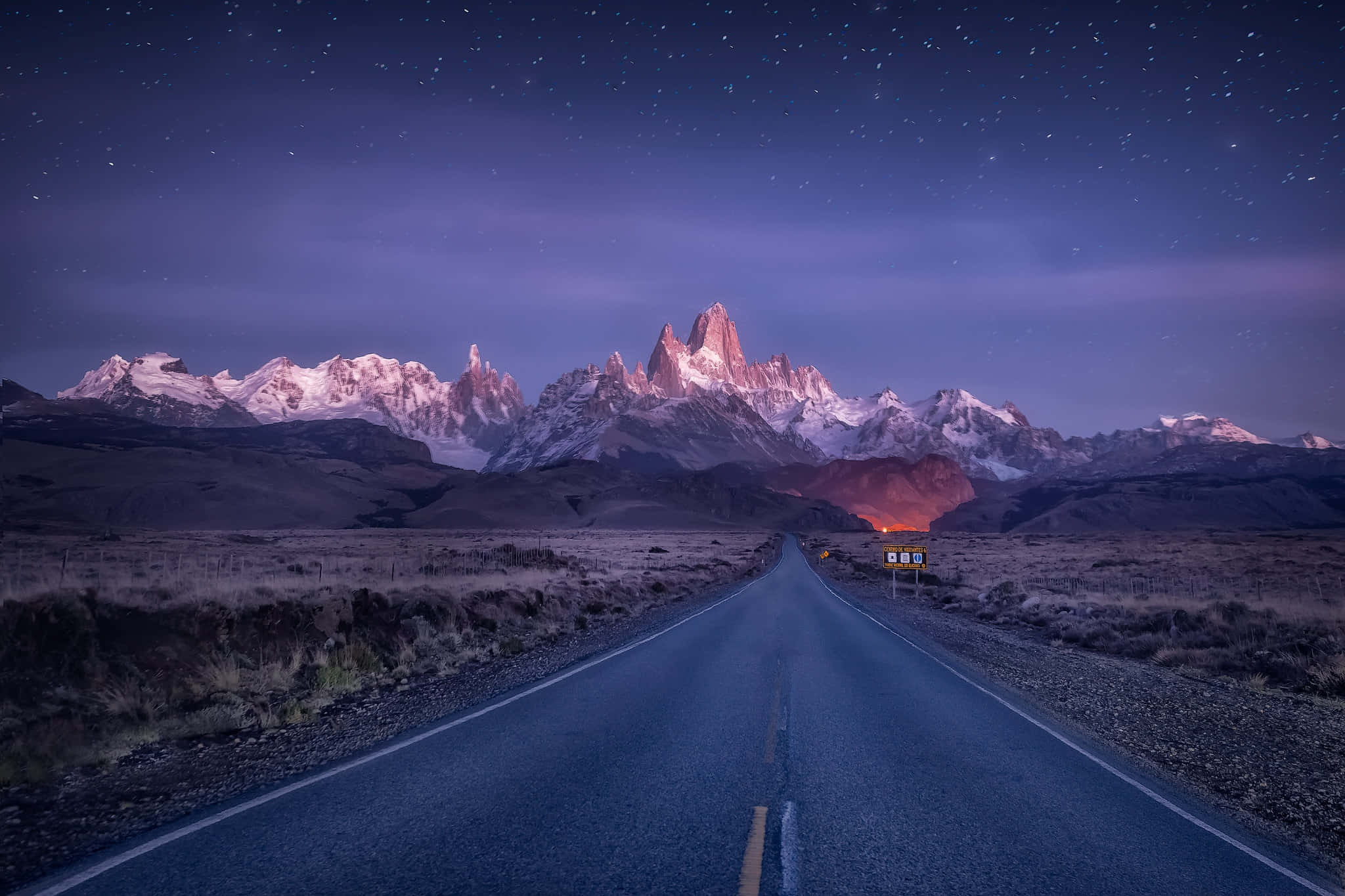 Patagonia 桌布 壁紙 — 星空下的夜空照亮了積雪的山脈，一條孤獨的道路延伸向山峰。