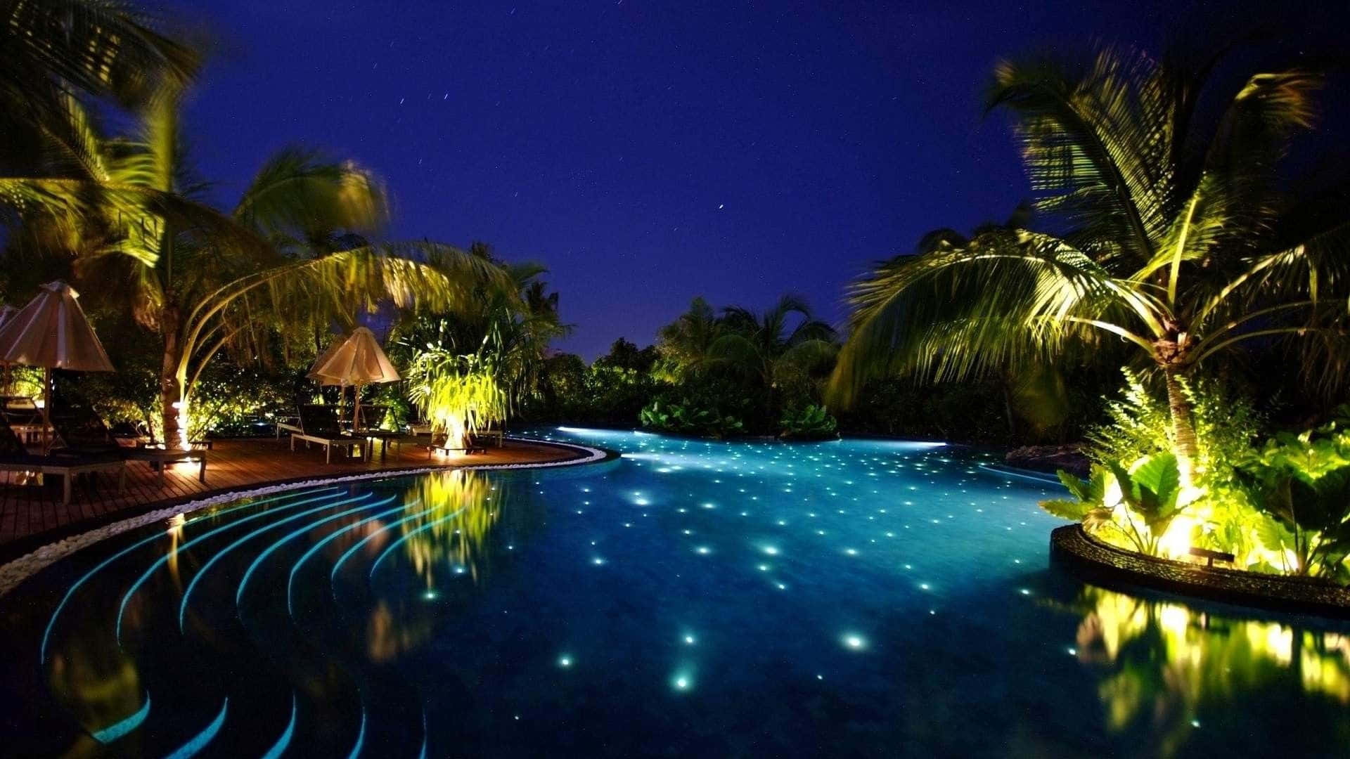 HD Beach 桌布 壁紙 — 星空下的無邊際泳池，在棕櫚樹和溫暖燈籠環繞的黑暗天空下，內置燈光閃爍。