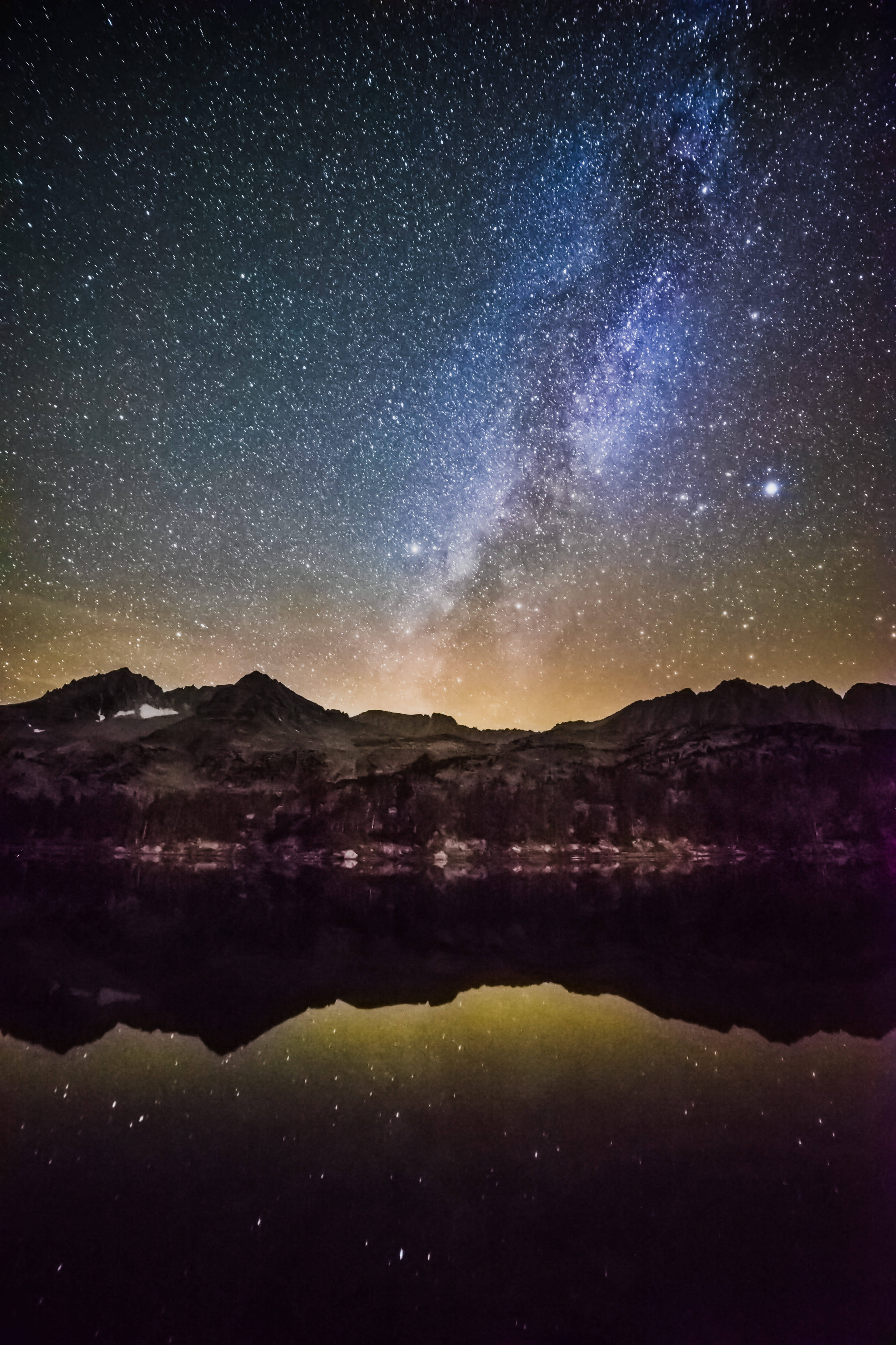 iPhone 桌布 壁紙 — 星空之夜，銀河拱橋在倒映於平靜湖面的剪影山脈之上。