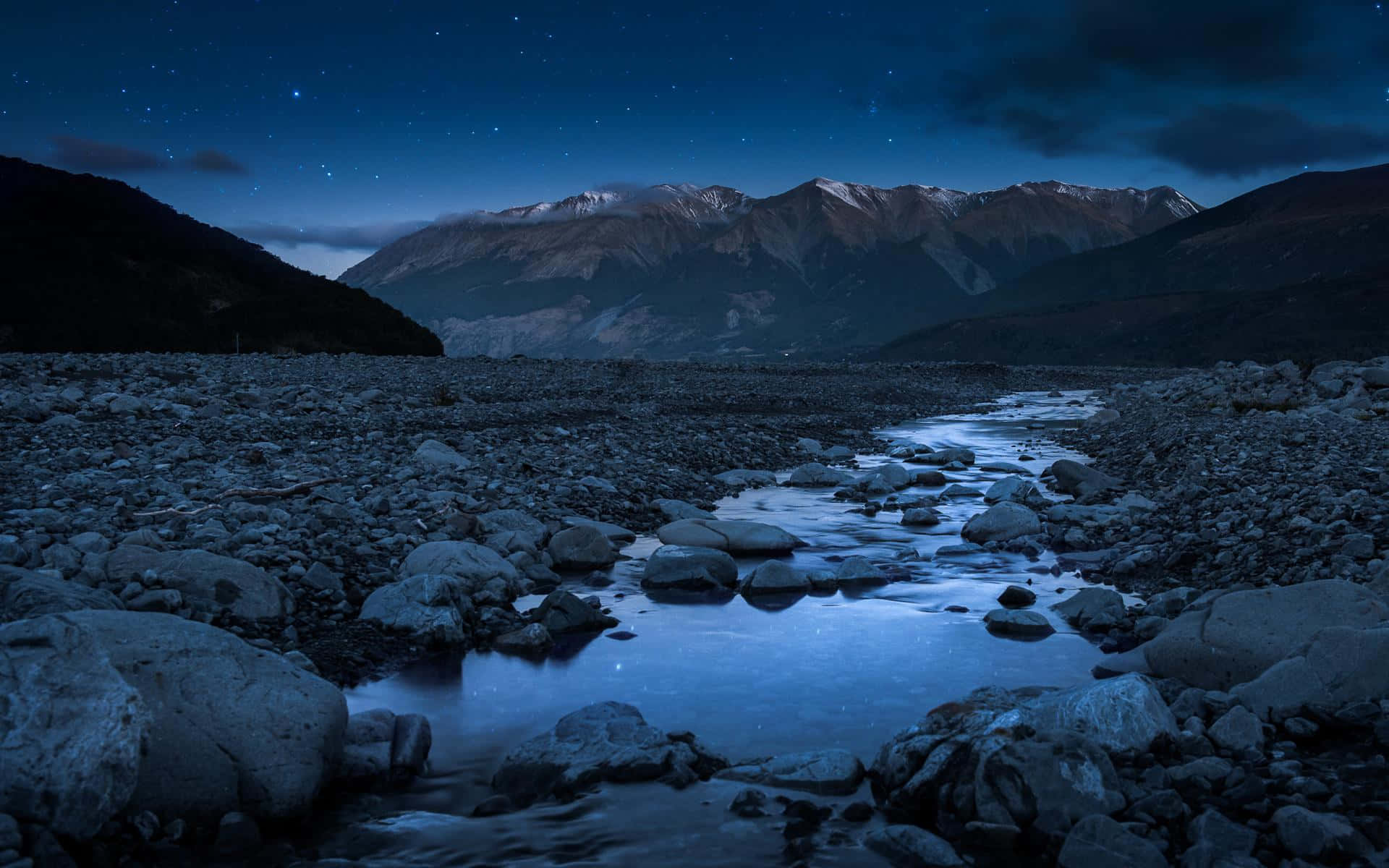 風景 桌布 壁紙 — 星空倒映在一條平靜的河流中，河流蜿蜒穿過一個岩石山谷，遠處有積雪覆蓋的山峰。