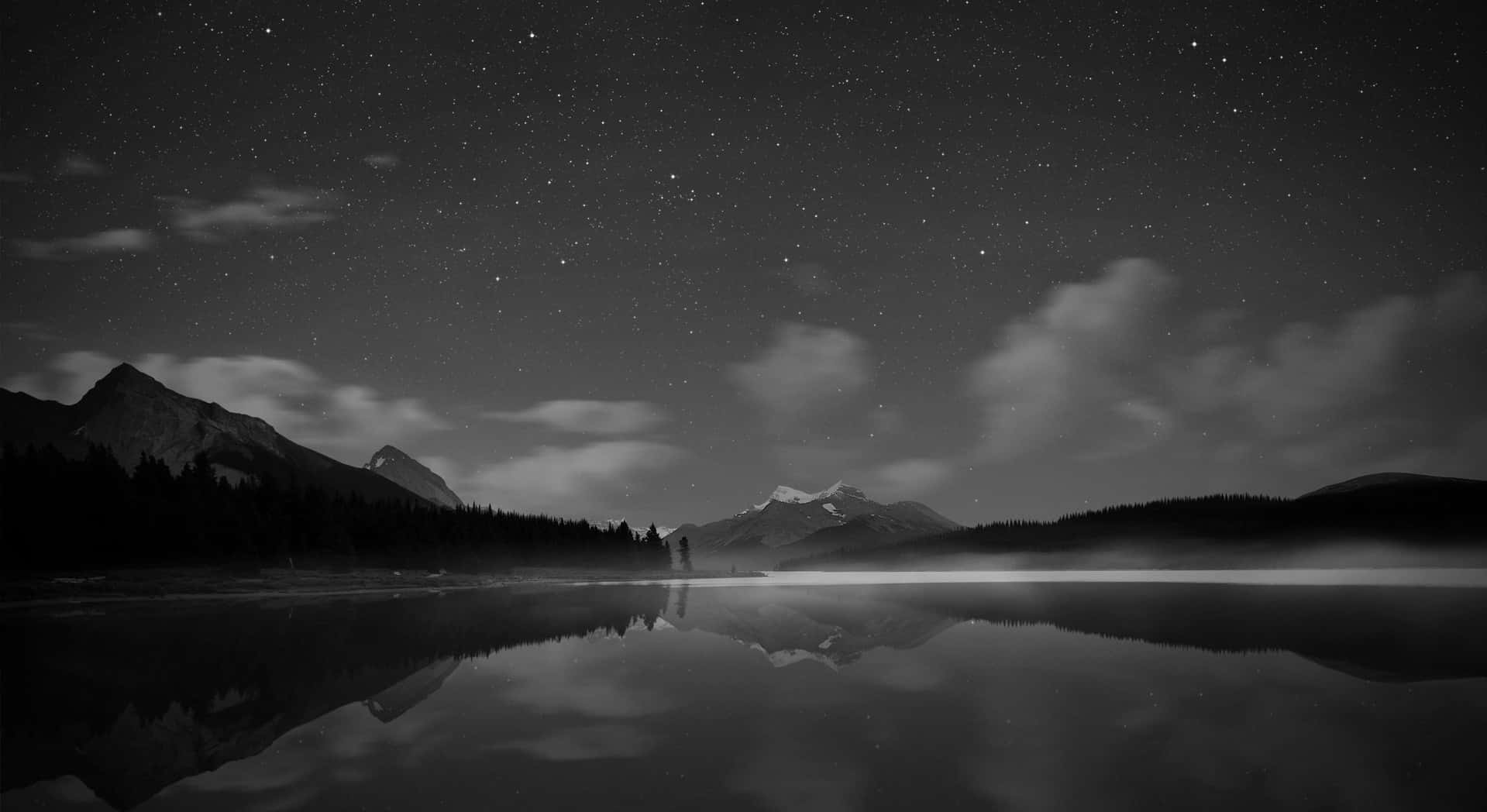 Monochrome 桌布 壁紙 — 星空在平靜的湖面上完美倒映，四周環繞著山脈和樹木的剪影。