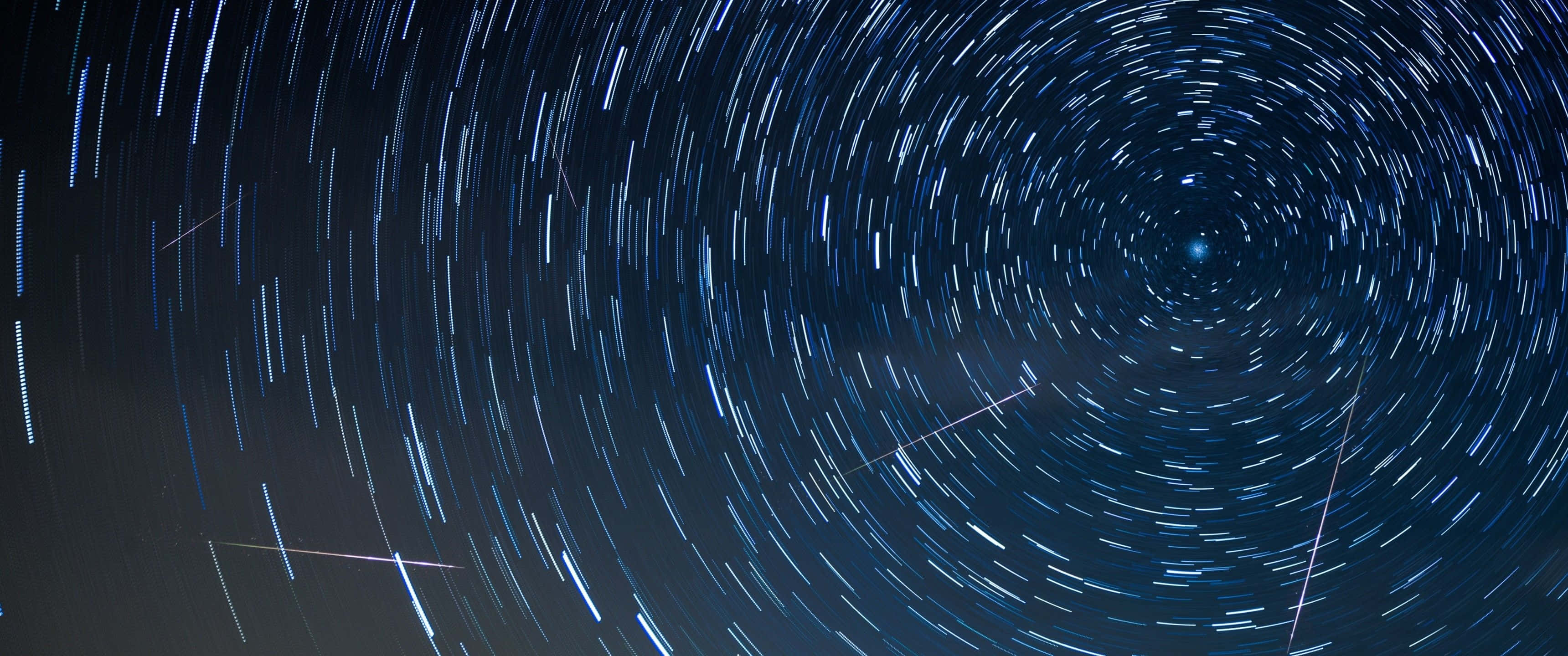地球 桌布 壁紙 — 星空夜空，有旋轉的藍白色星軌從中心點向黑暗宇宙背景輻射。