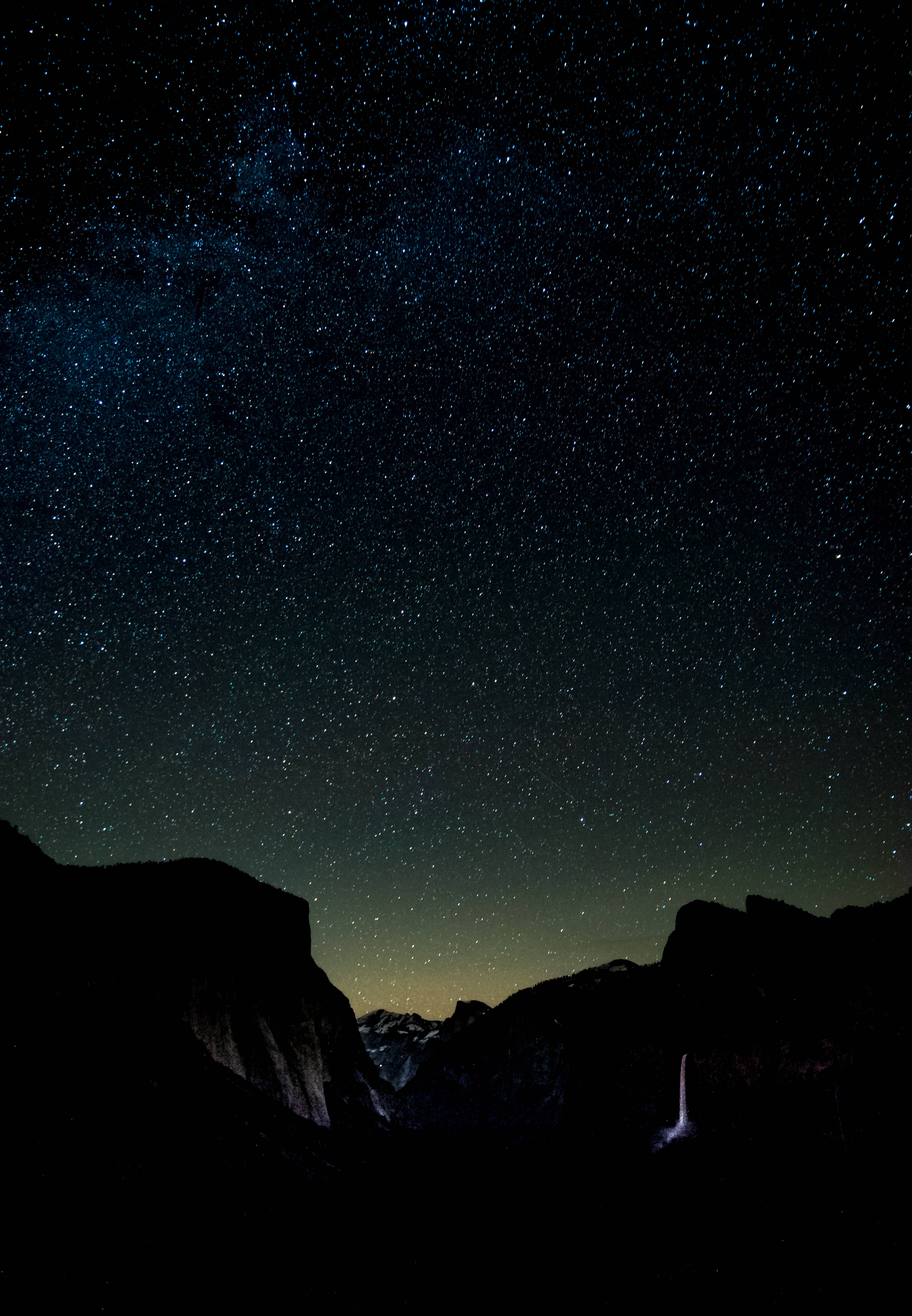iPhone 11 dark 桌布 壁紙 — 星空夜空，銀河在黑暗山脈輪廓和下方發光瀑布上方拱起。