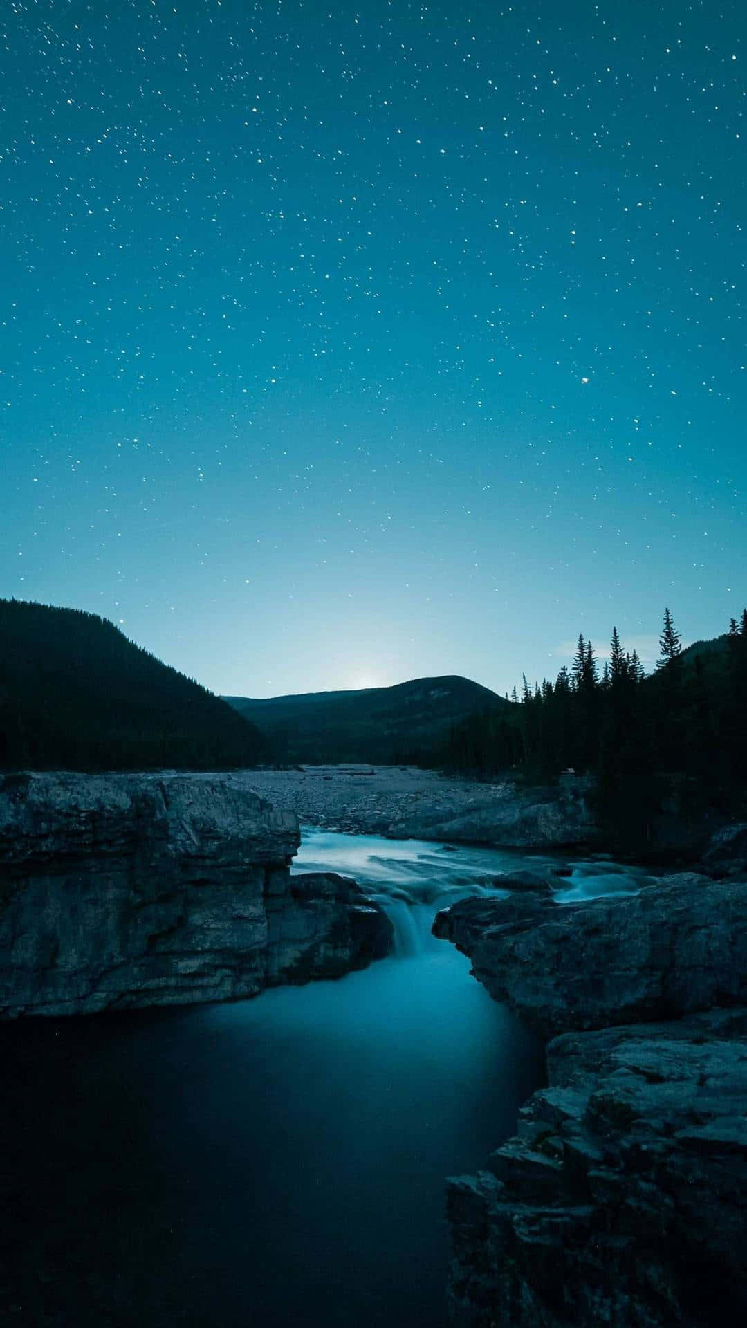 自然 桌布 壁紙 — 星空夜空在寧靜的河流上方閃耀，流經岩石地形，遠處有山脈和松樹。
