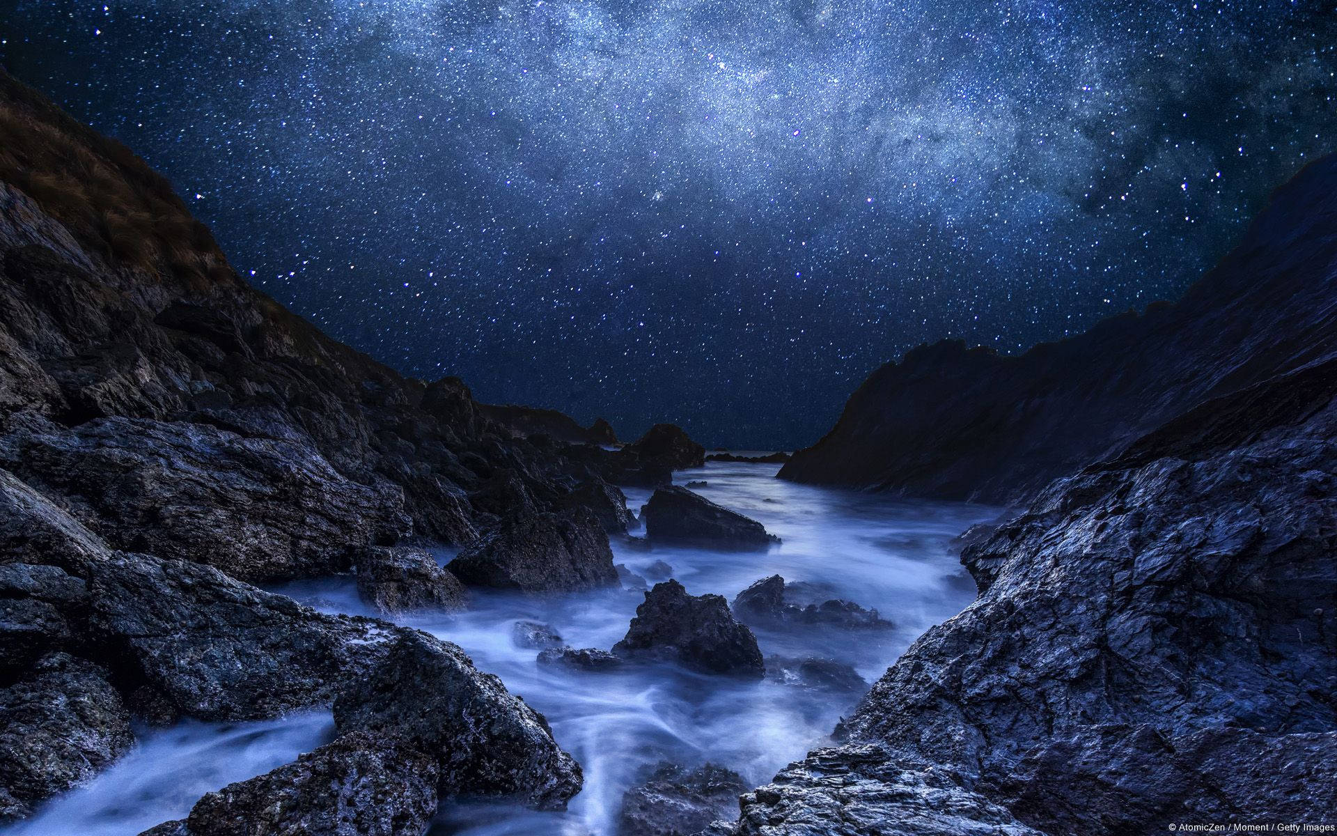 岩石海岸線上的星空夜空，帶有發光的藍色海洋波浪。 — Microsoft 壁紙