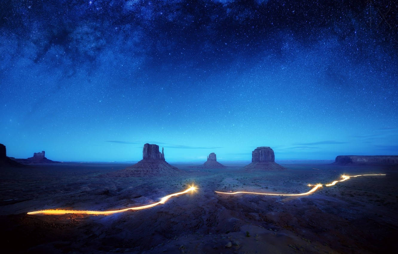 Arizona 桌布 壁紙 — 星空夜空拱形籠罩紀念碑谷的標誌性岩柱，發光的光跡蜿蜒穿過沙漠地面。