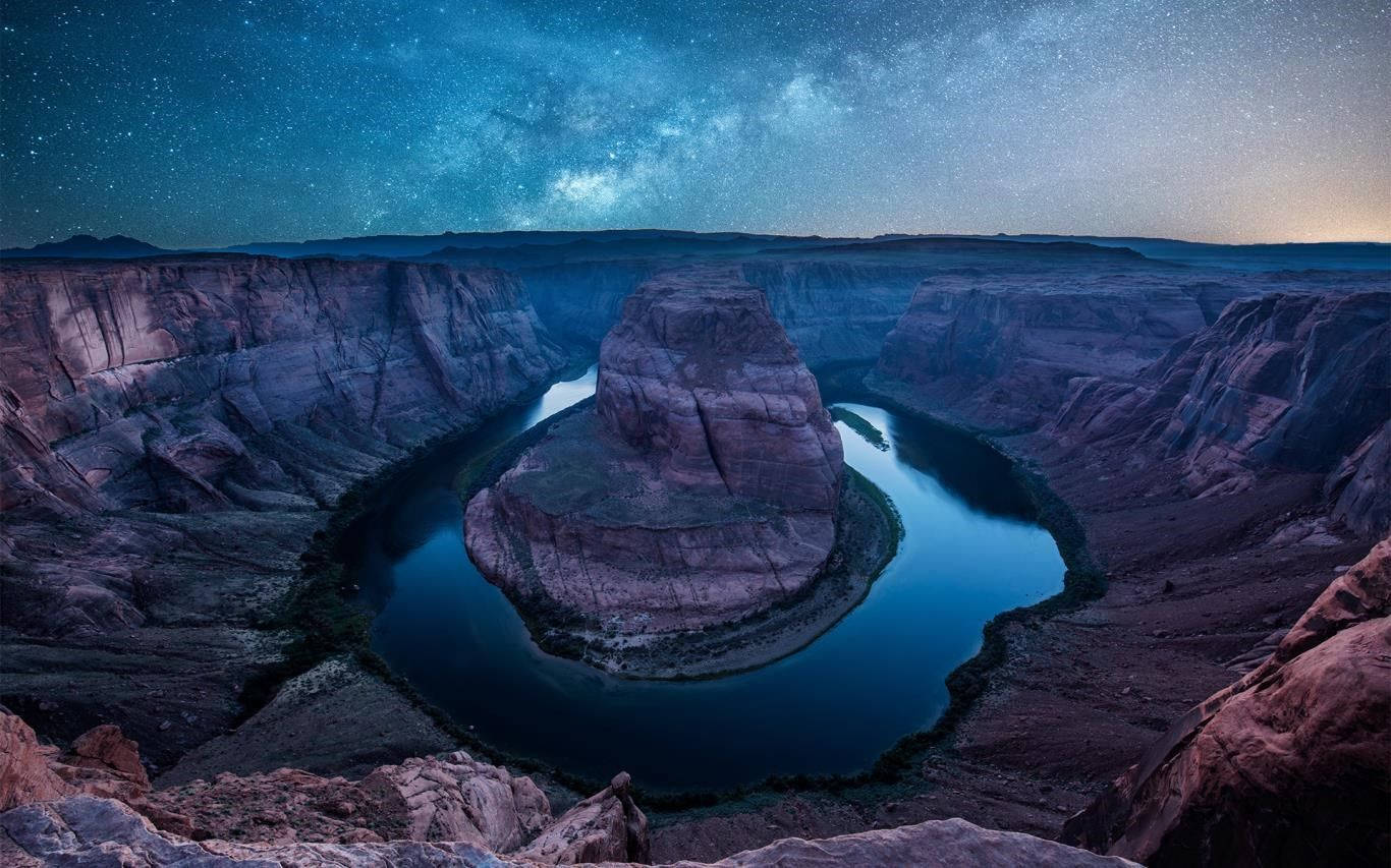 在星空下，河流蜿蜒繞過峽谷中的一塊大岩石。 — Microsoft 壁紙