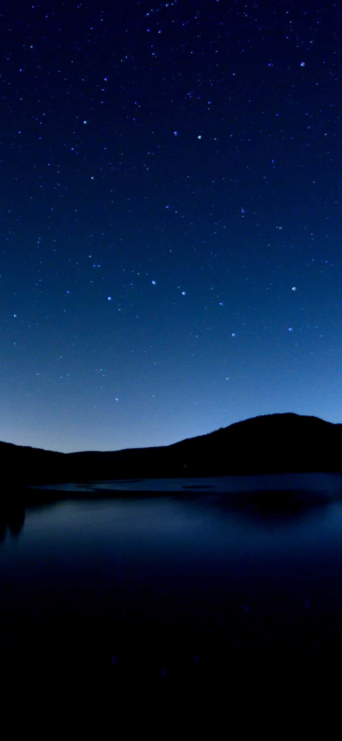 iPhone 桌布 壁紙 — 星空夜空映照在平靜的湖面上，下方是黑暗的剪影山丘。
