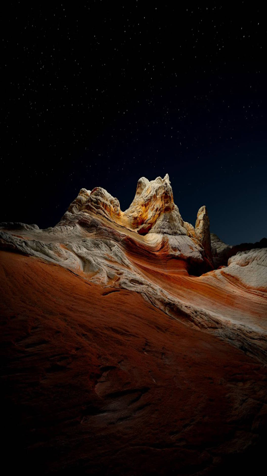 iOS 桌布 壁紙 — 星空夜空照亮了崎嶇的層狀岩層，以溫暖的橙色和白色色調映襯著深紅色的沙漠沙地。