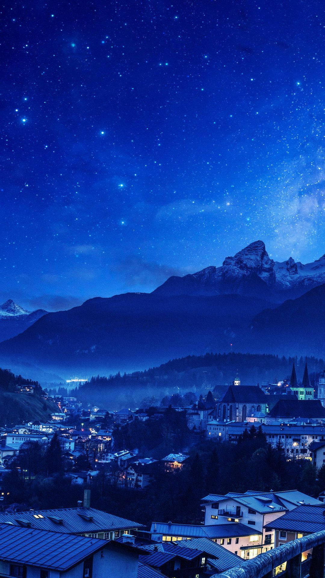 山景 桌布 壁紙 — 星空夜空覆蓋著一個山城，窗戶發光，下方是積雪的山峰。