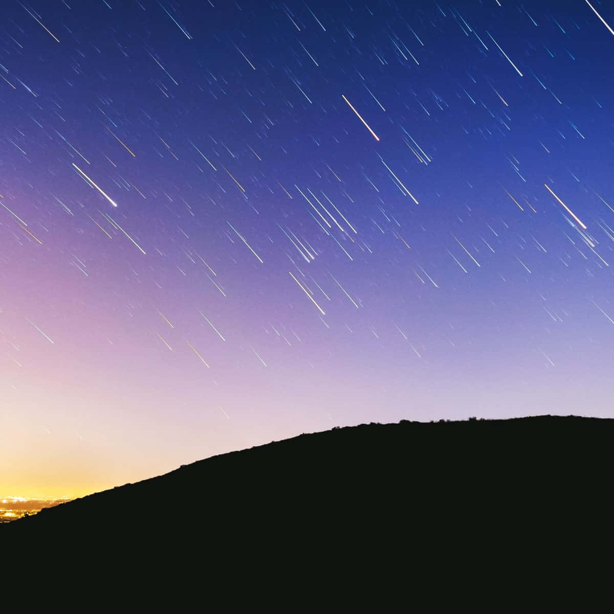 meteor 桌布 壁紙 — 星軌劃過暮色天空，在黑暗山丘剪影之上，遠方城市燈光在地平線閃爍。