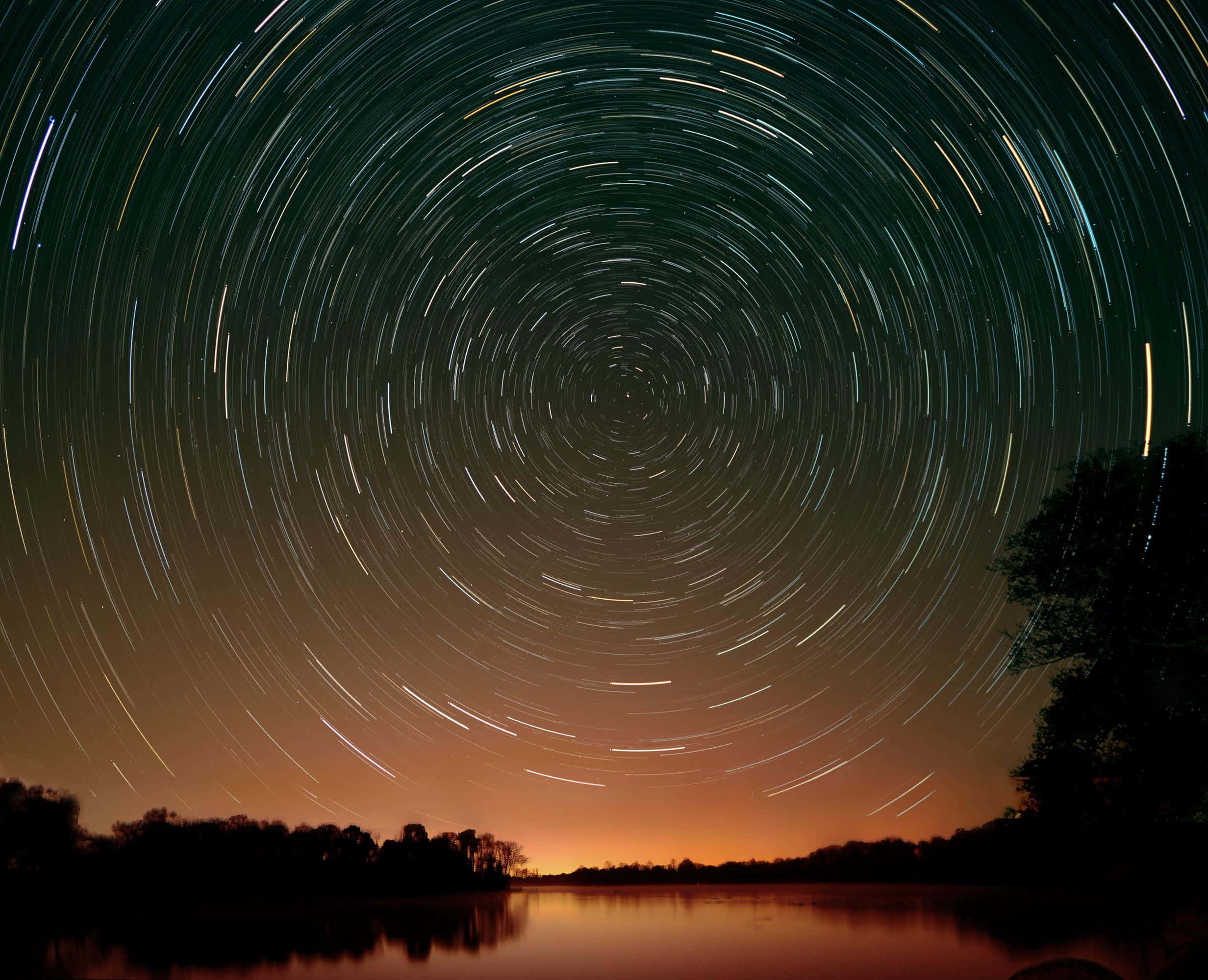 Astrophysics 桌布 壁紙 — 星軌在寧靜河流上方的暮色天空中形成同心圓弧，河流反射出橙色和深綠色調。