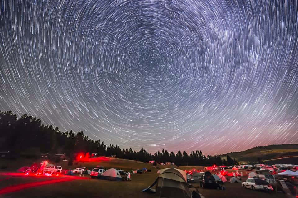South Pole 桌布 壁紙 — 星軌在暮色中戲劇性地盤旋在一個佈滿帳篷和發光紅燈的營地上空。
