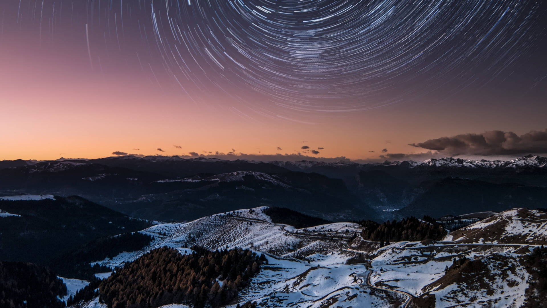 冬季美學 桌布 壁紙 — 星軌在暮色天空中劃過，下方是積雪的山脊和森林覆蓋的山谷。