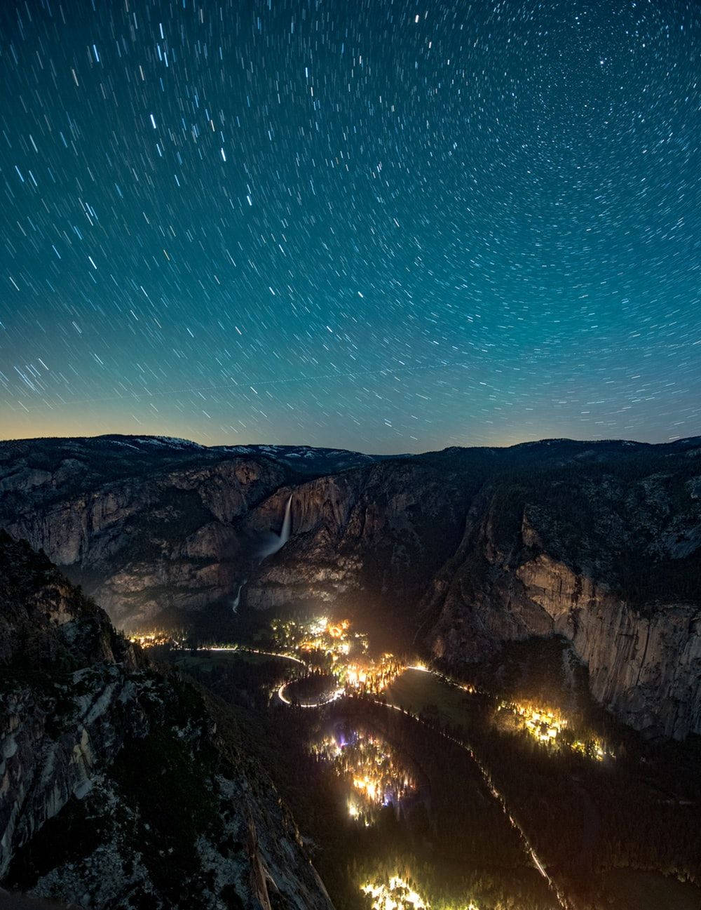 Screen 桌布 壁紙 — 星軌在深藍色夜空上劃過，下方是被雪覆蓋的峽谷山谷，溫暖的村莊燈火閃爍。