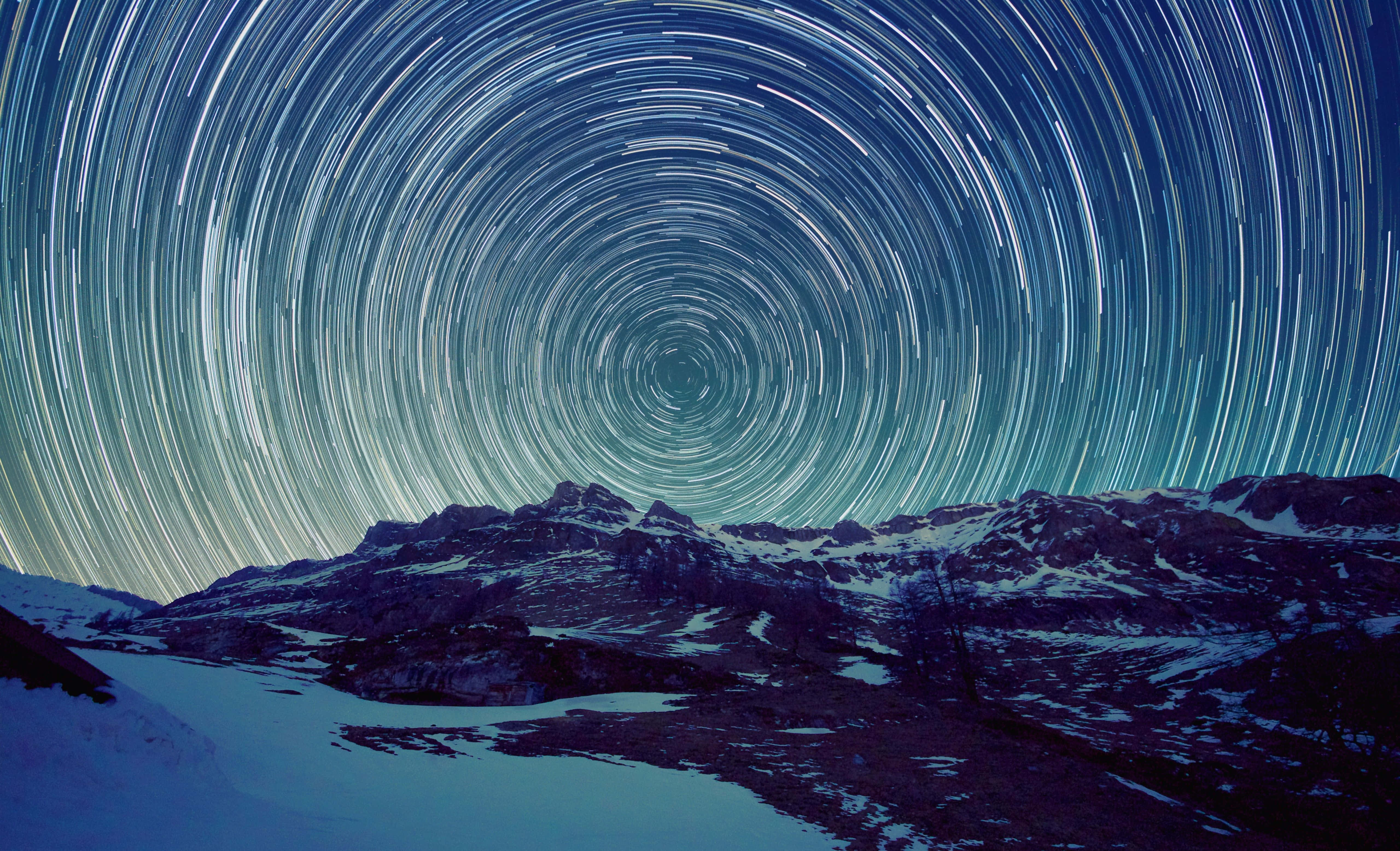 Stars 桌布 壁紙 — 星軌在深藍色夜空下，在積雪的山脈上方盤旋成催眠般的弧線。
