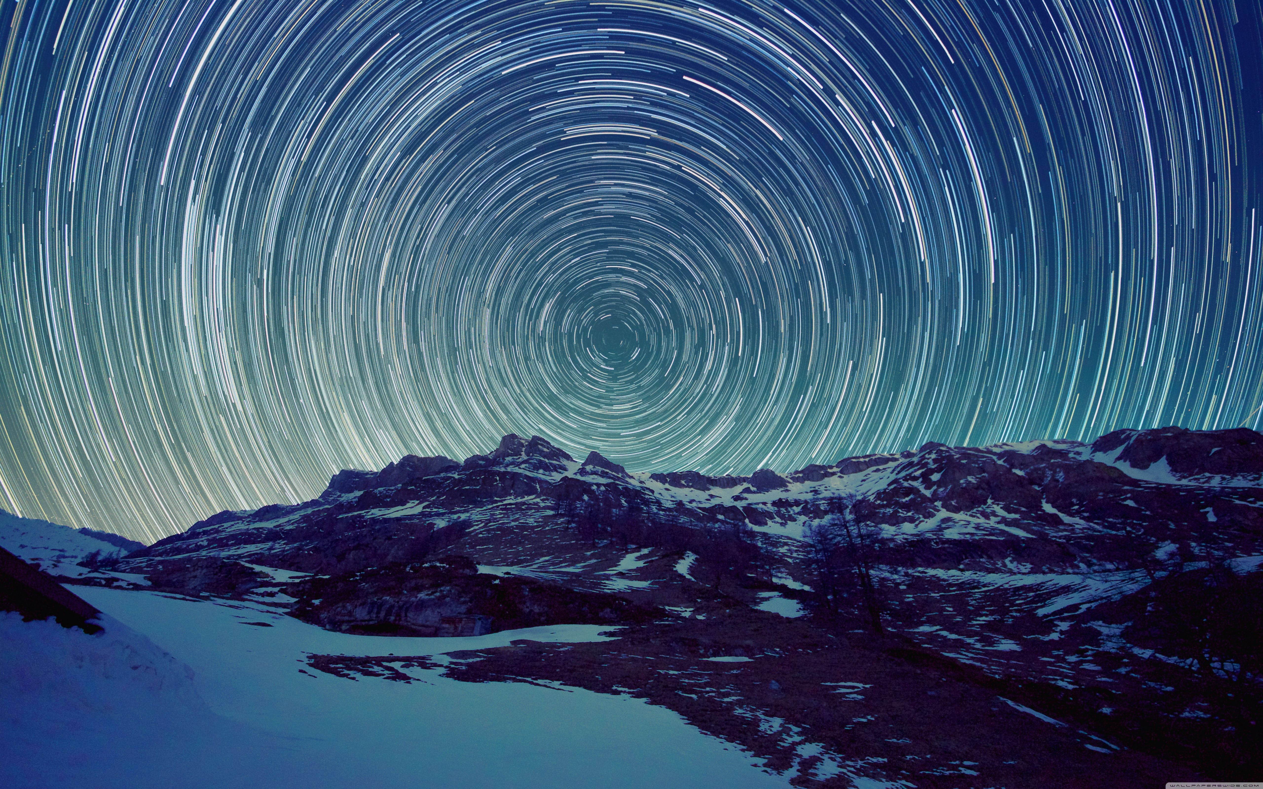 Stars 桌布 壁紙 — 星軌在深藍色夜空下，戲劇性地盤旋在覆蓋著雪的山脈之上。