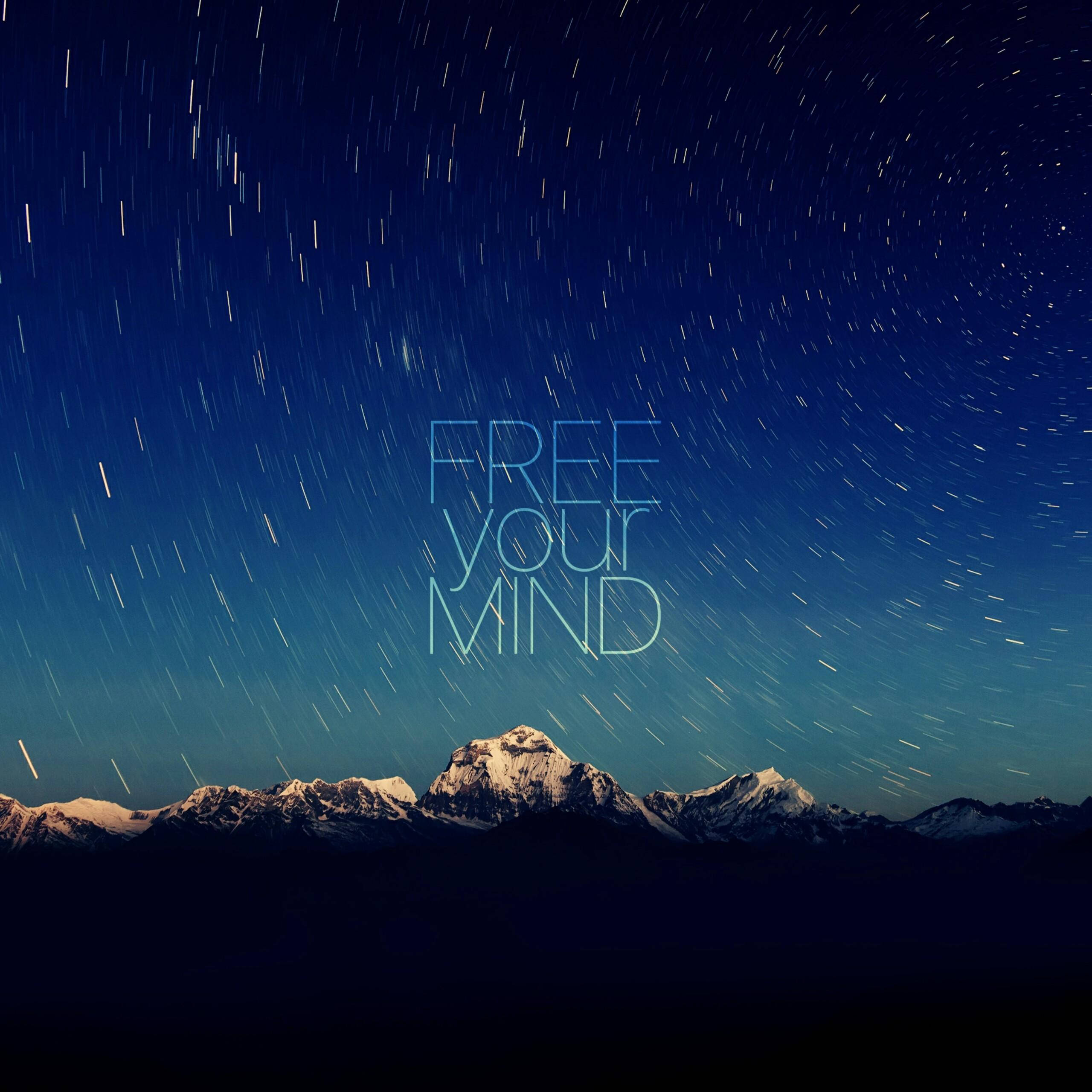 語錄 桌布 壁紙 — 星軌在深藍色夜空下的雪山上方旋轉，free your mind 文字柔和發光。