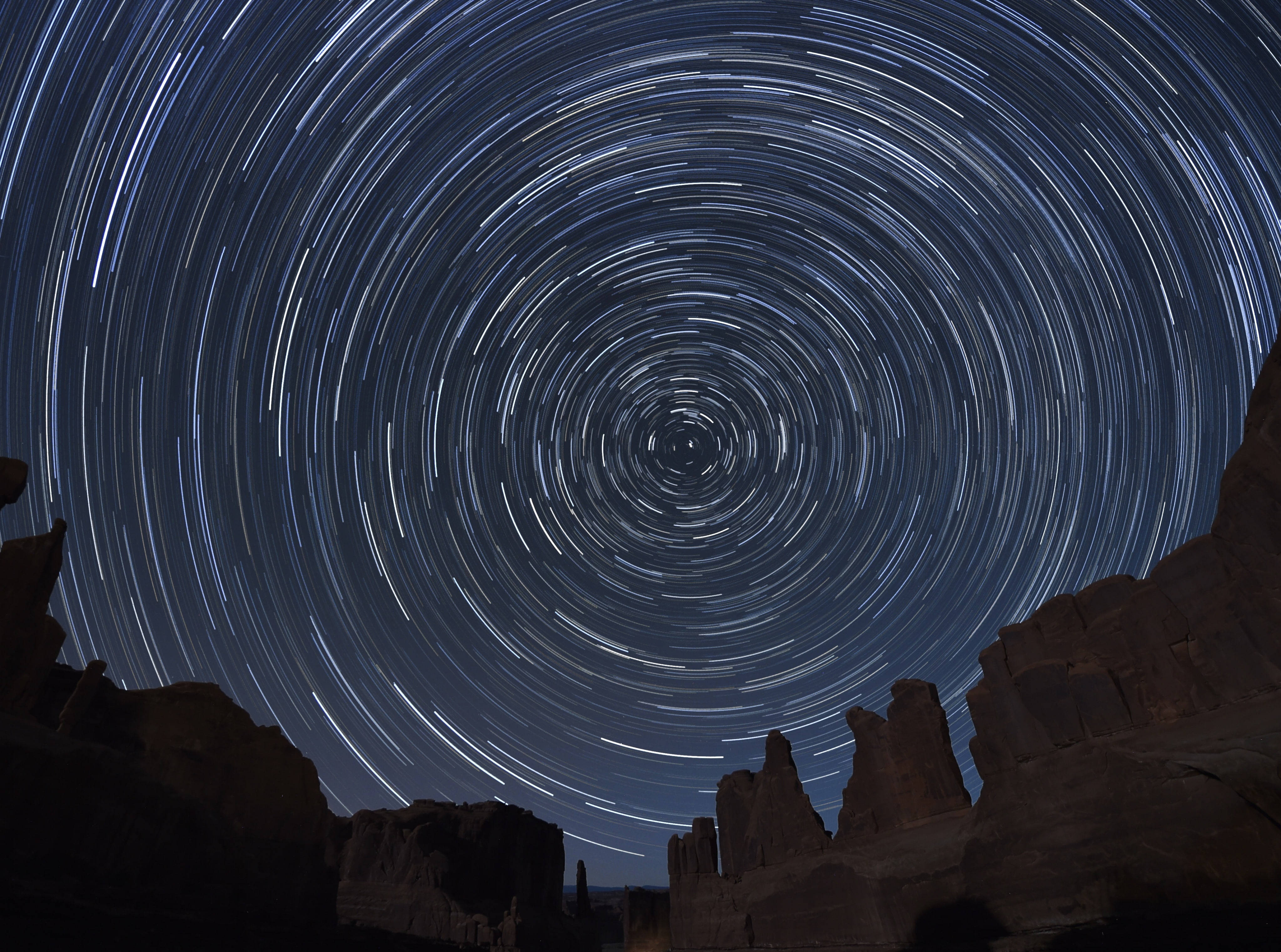 Stars 桌布 壁紙 — 星軌在深藍色夜空中戲劇性地螺旋，籠罩著崎嶇的沙漠岩石地貌。