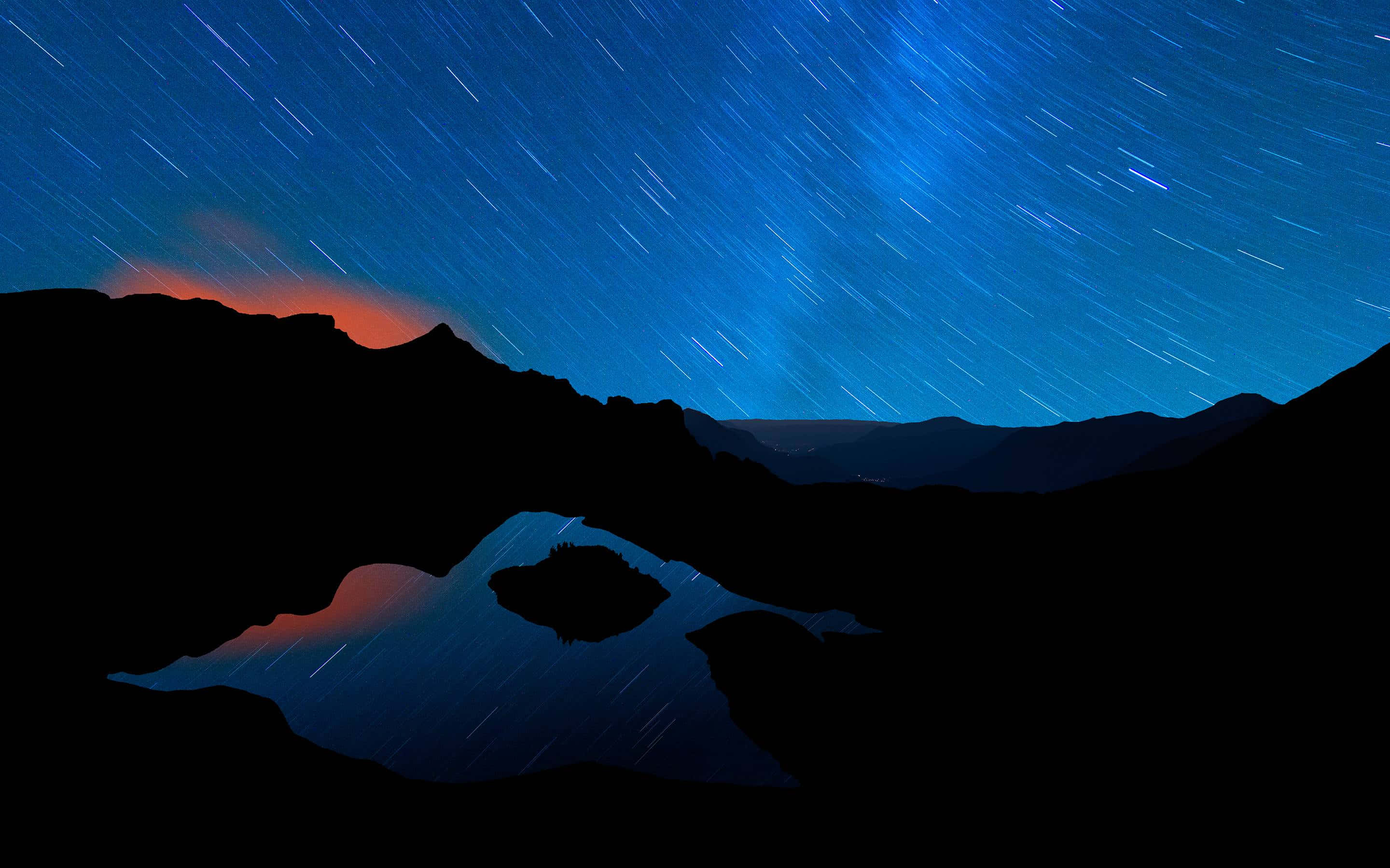銀河 桌布 壁紙 — 星軌在深藍色的夜空中劃過，映襯著剪影般的山脈和反射著橙色極光的湖泊。