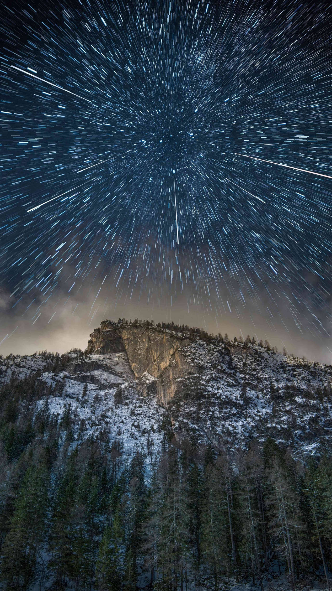 桌布 壁紙 — 星軌在白雪覆蓋的山峰和松樹林上方漆黑的冬日天空中劃過。