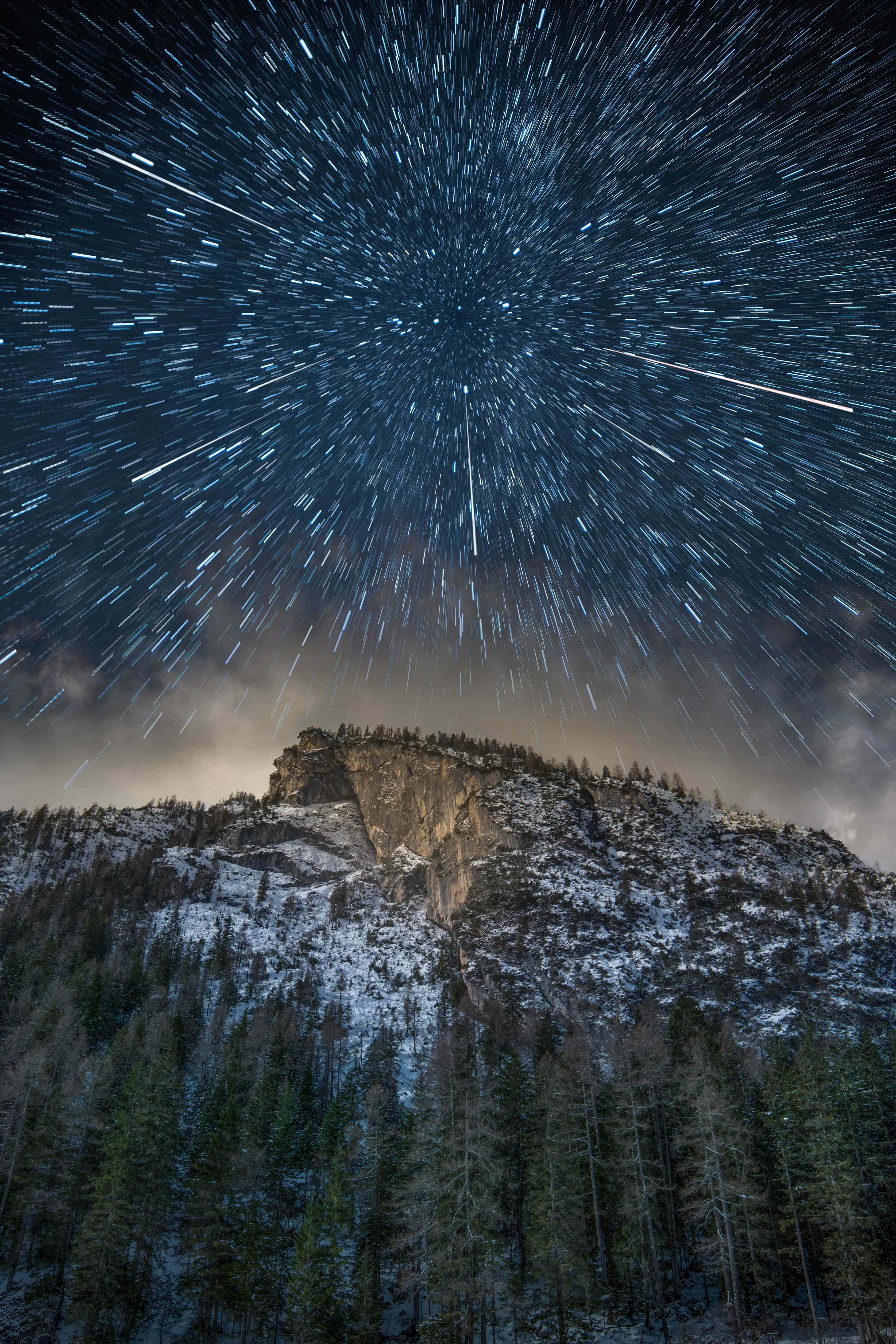 圖片 桌布 壁紙 — 星軌在黑暗的冬季天空中劃過，下方是積雪的山峰和松樹林。