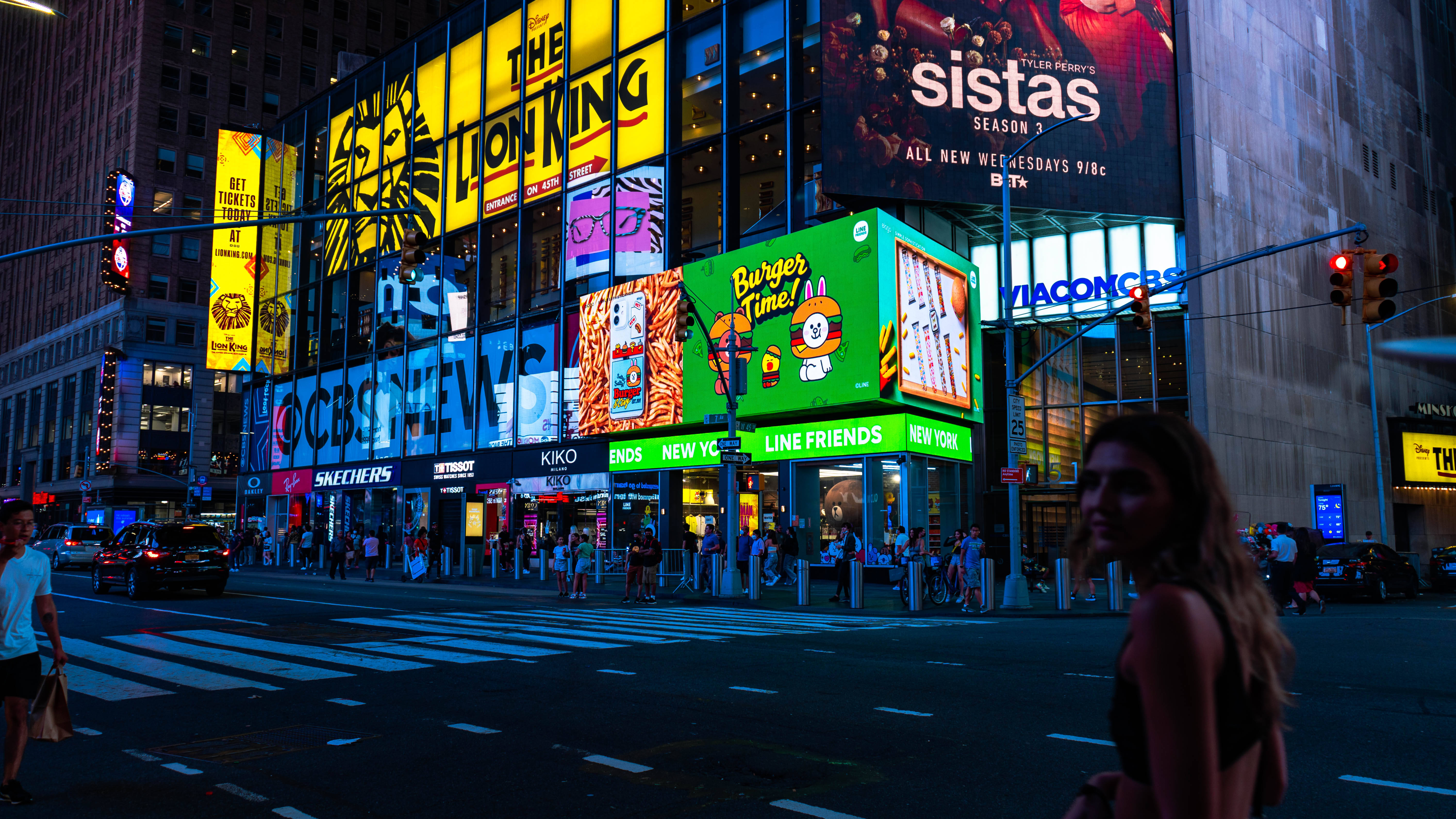 Nyc Aesthetic 桌布 壁紙 — 時代廣場充滿活力的夜景，發光的廣告牌宣傳獅子王和Sistas，行人過馬路，明亮的霓虹燈照亮高聳的建築物。