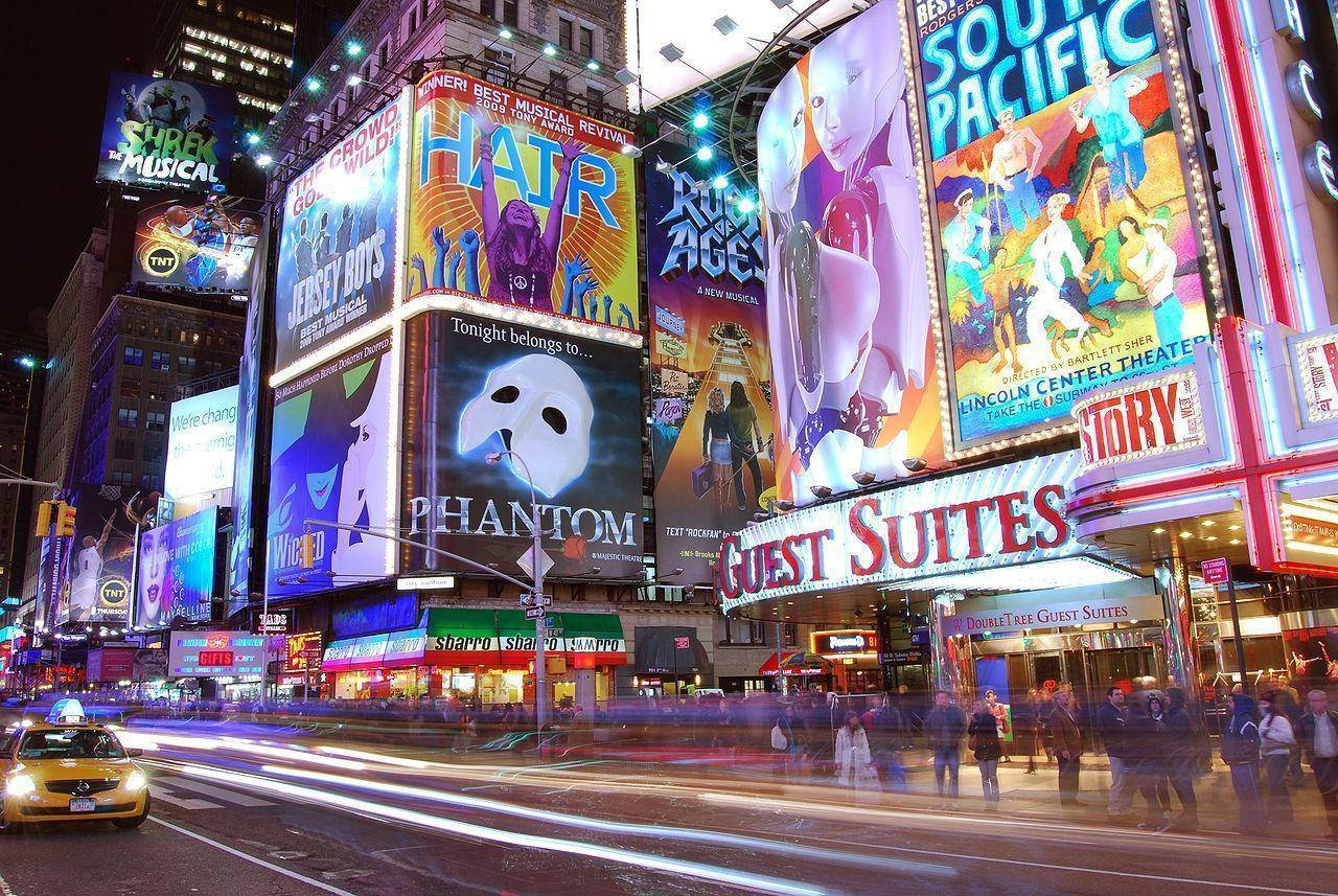 Broadway 桌布 壁紙 — 時代廣場充滿活力的夜景，閃耀的百老匯廣告牌和飛馳的計程車燈光。
