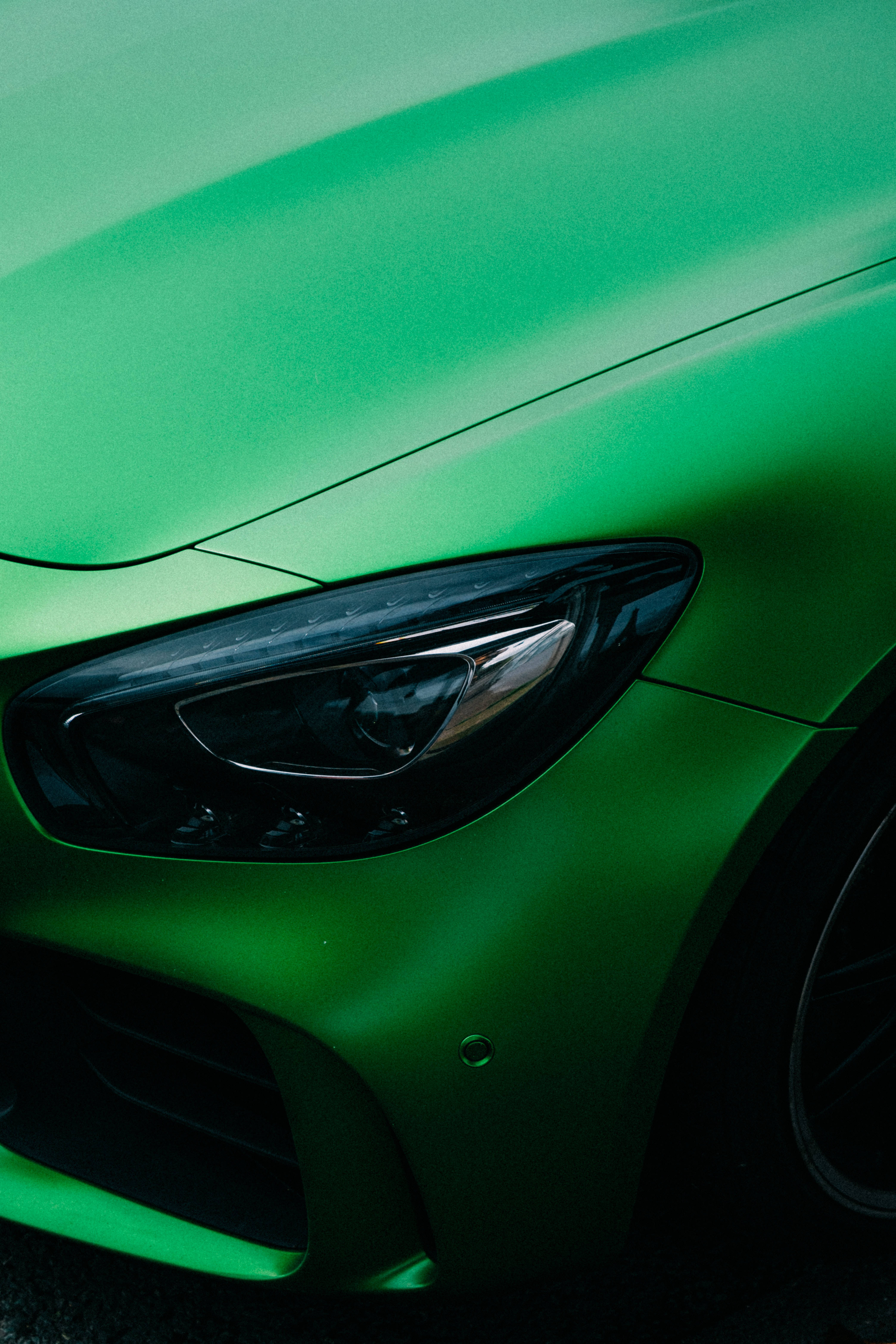 mercedes amg iPhone 桌布 壁紙 — 時尚消光綠色跑車頭燈和引擎蓋的特寫，線條銳利，表面反光。