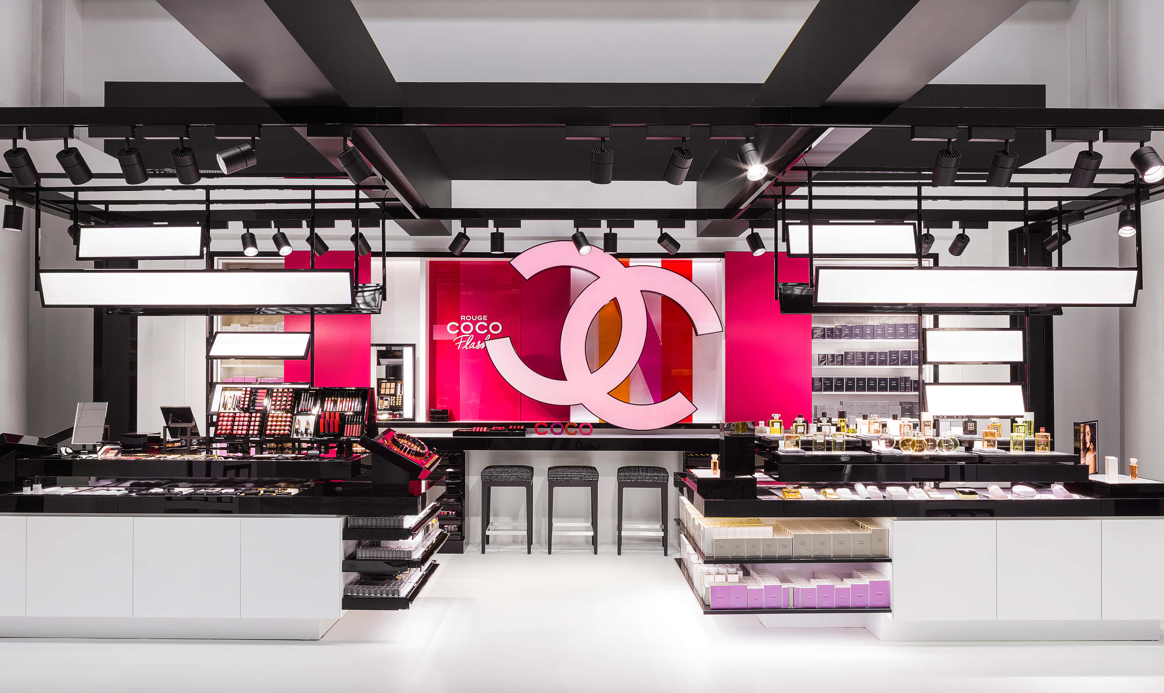 Chanel 桌布 壁紙 — 時尚現代的 Chanel 化妝品精品店，採用大膽的粉紅色品牌、黑色裝置和明亮的聚光燈照亮產品展示。