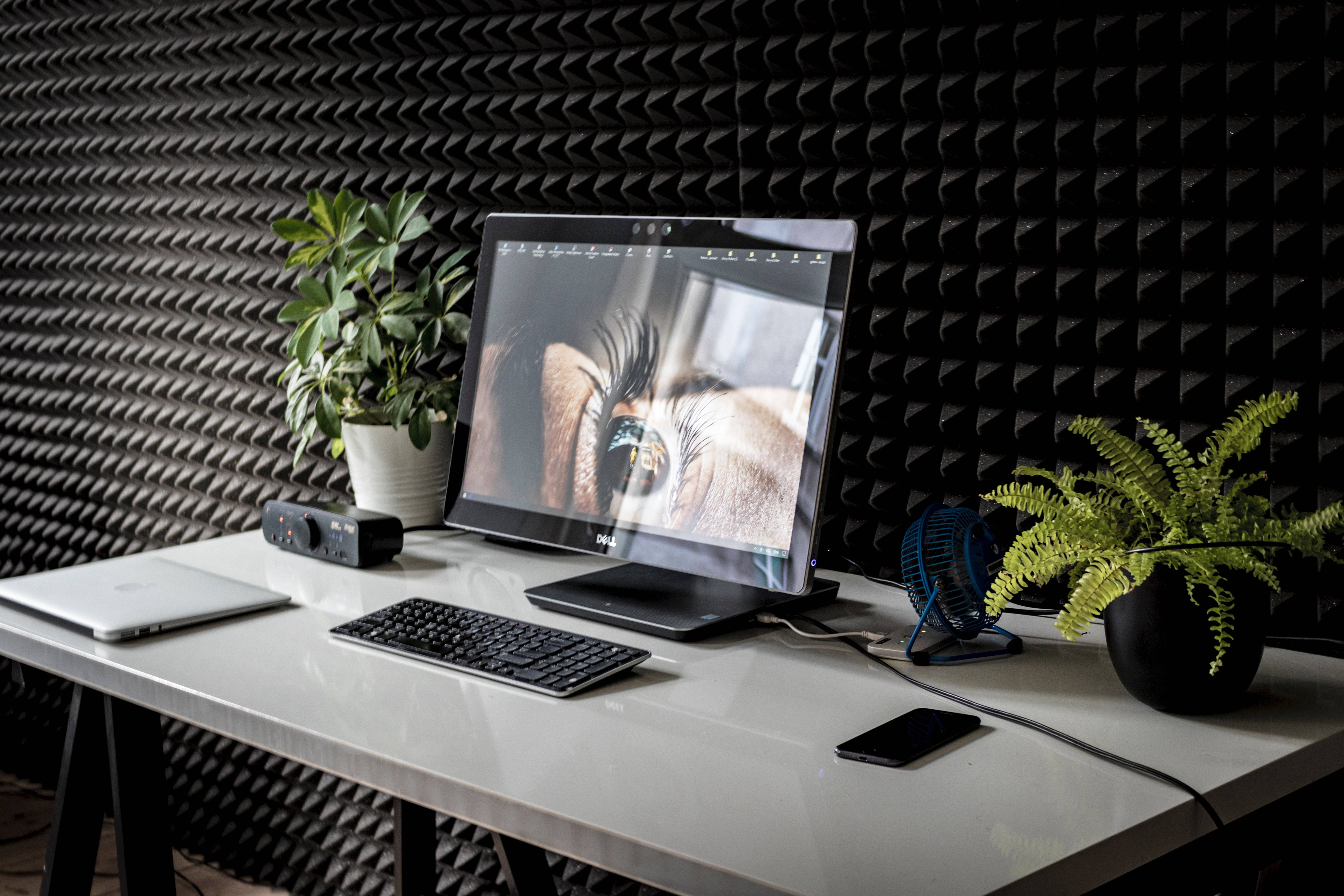 Desk 桌布 壁紙 — 時尚白色書桌，顯示器展示眼睛特寫，兩側有綠色植物，背景為黑色隔音牆。