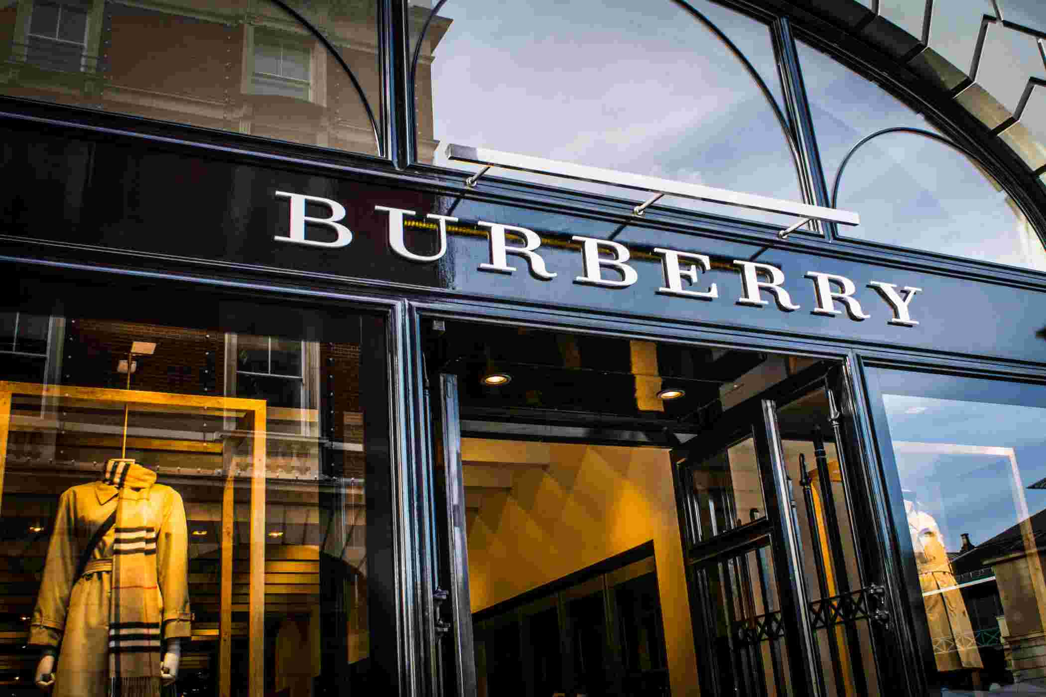 Burberry 桌布 壁紙 — 時尚的 Burberry 店鋪外牆，配有玻璃門和經典風衣模特兒，在溫暖的室內燈光下展示。
