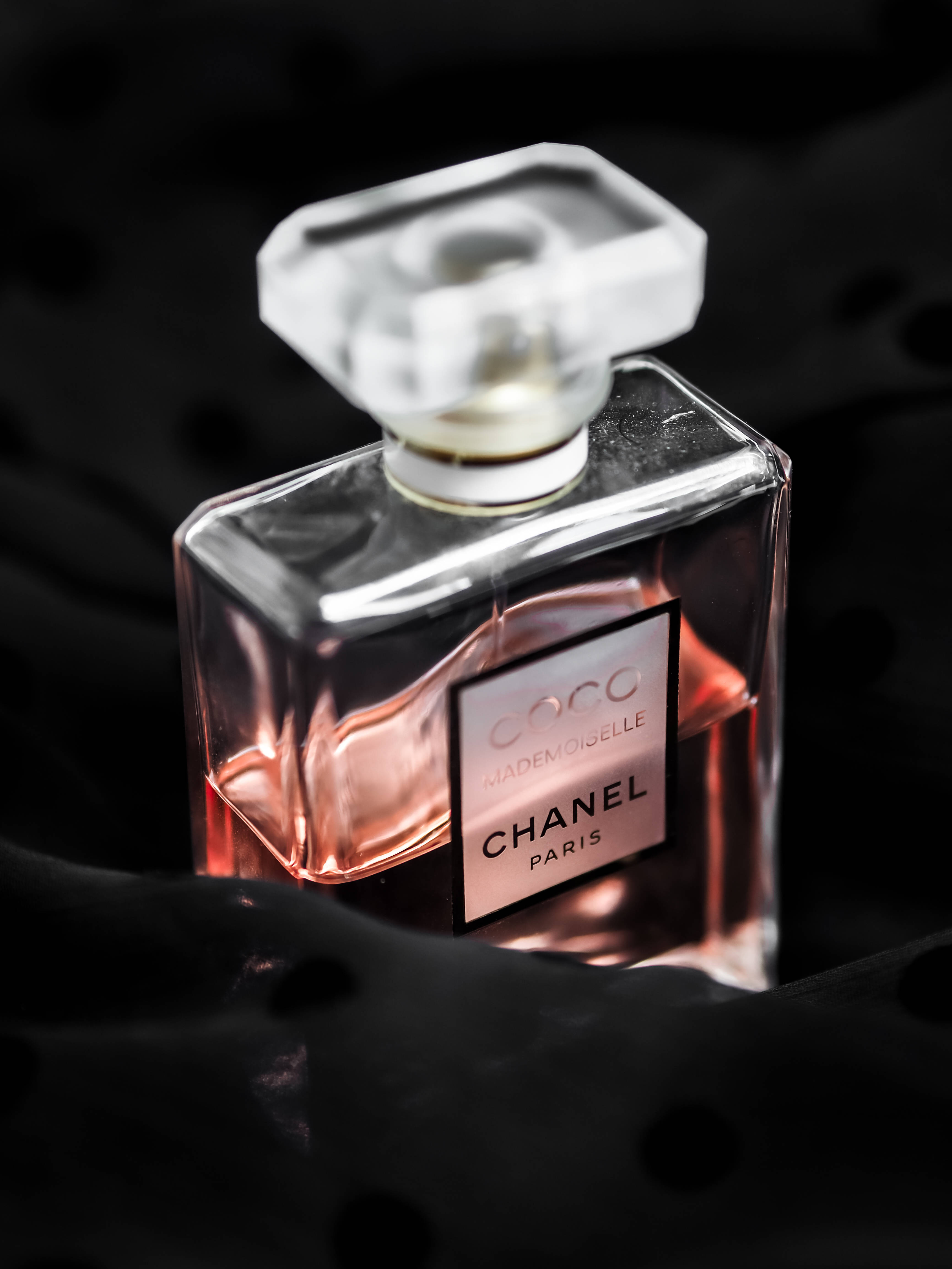 Chanel 桌布 壁紙 — 時尚的 Chanel Coco Mademoiselle 香水瓶在柔軟的黑色布料背景下閃耀著玫瑰色液體。