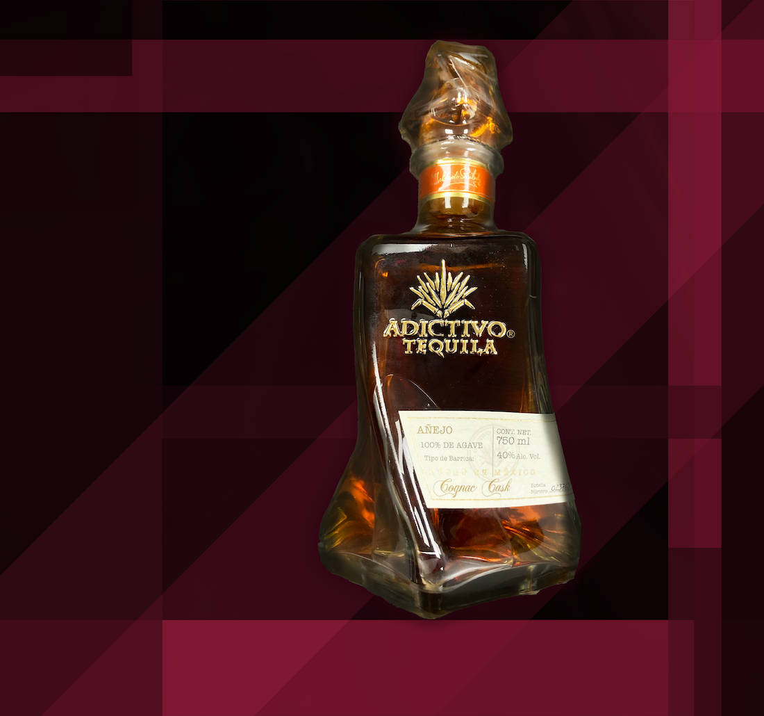 高清 桌布 壁紙 — 時尚的Adictivo Tequila Añejo酒瓶在搶眼的幾何酒紅色和黑色背景上閃耀著琥珀色液體。
