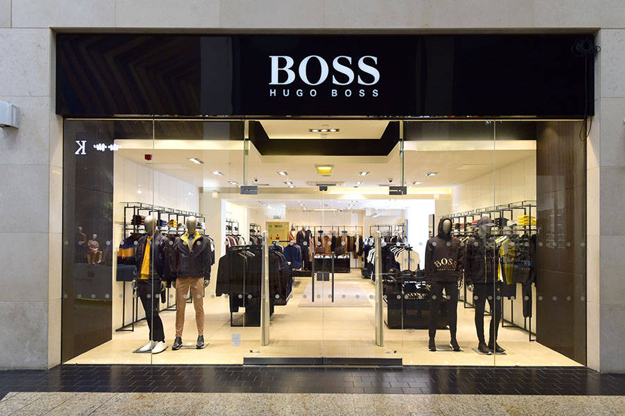 Clothes 桌布 壁紙 — 時尚的Hugo Boss店鋪正面，玻璃門和模特兒在明亮的室內燈光下展示時尚男裝。