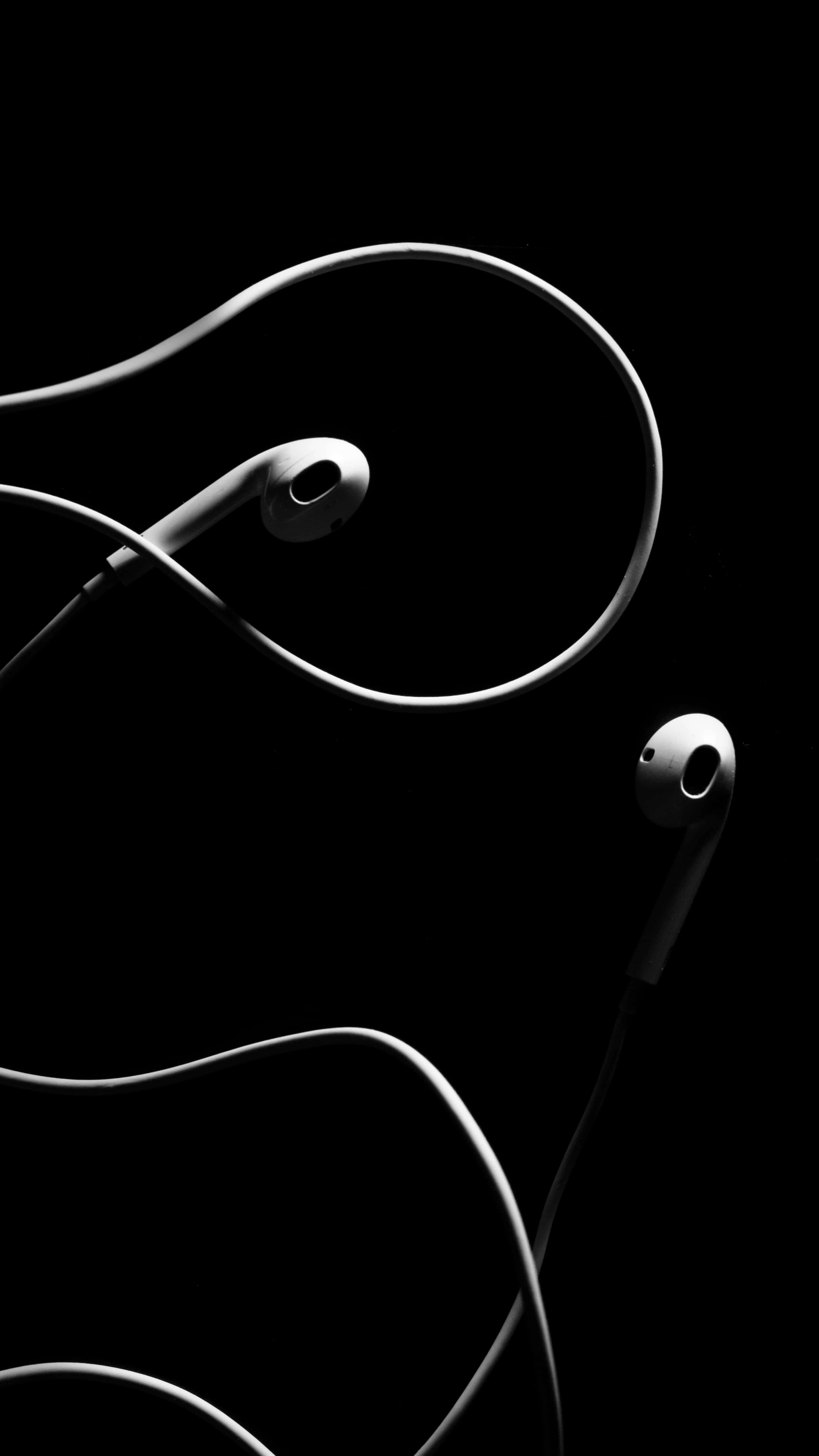 黑色 iPhone 桌布 桌布 壁紙 — 時尚的白色耳塞搭配螺旋線纜，在純黑背景上優雅彎曲，呈現高對比度的單色效果。