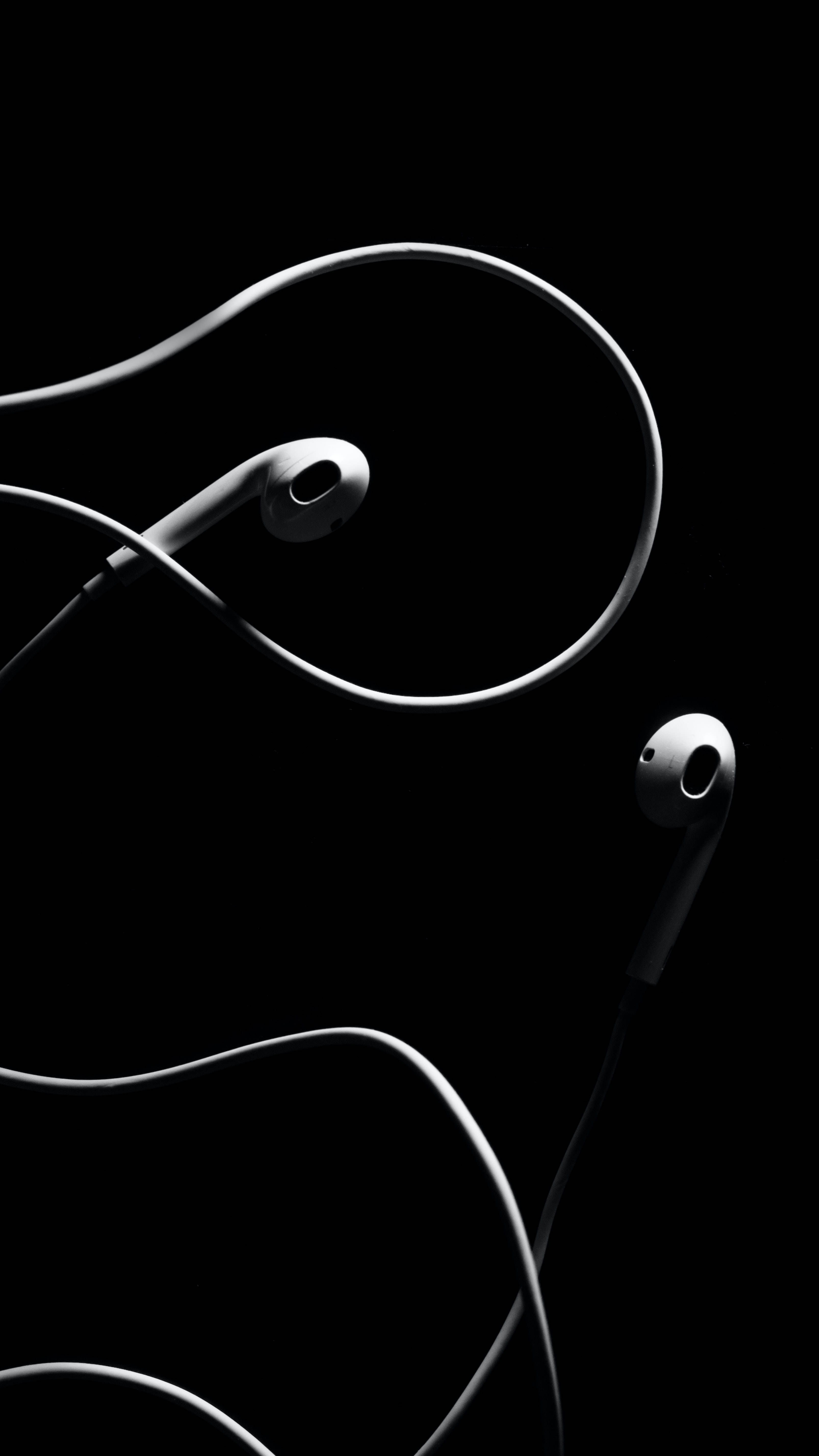 黑色 iPhone 桌布 桌布 壁紙 — 時尚的白色耳塞配彎曲電纜，在純黑色背景上以高對比度單色優雅地漂浮。