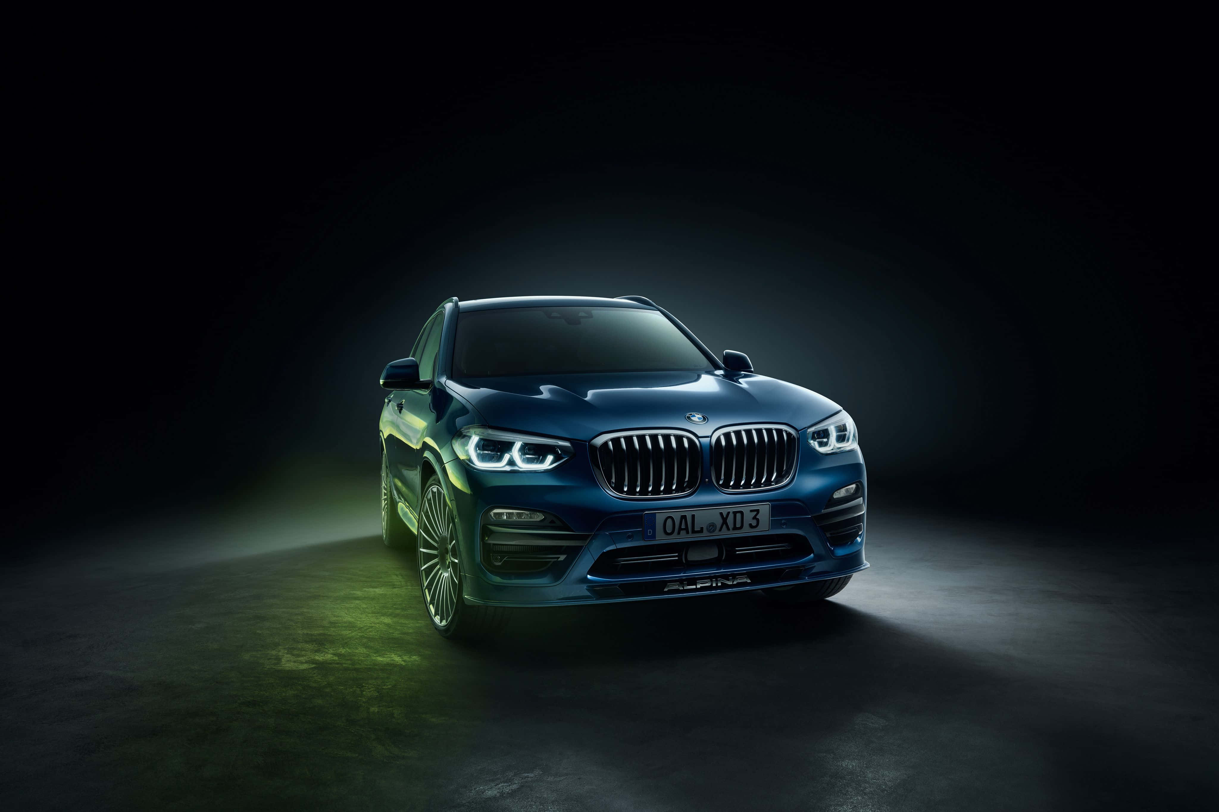 Bmw X3 桌布 壁紙 — 時尚的藍色BMW X5 Alpina在黑暗的攝影棚背景下，搭配綠色地板光芒，在戲劇性的聚光燈下閃耀。