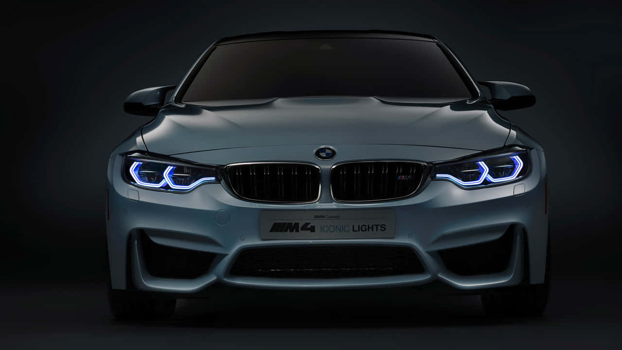 720p Bmw 桌布 壁紙 — 時尚的銀色BMW M4跑車在黑暗的攝影棚背景下散發出充滿活力的藍色LED頭燈光芒。