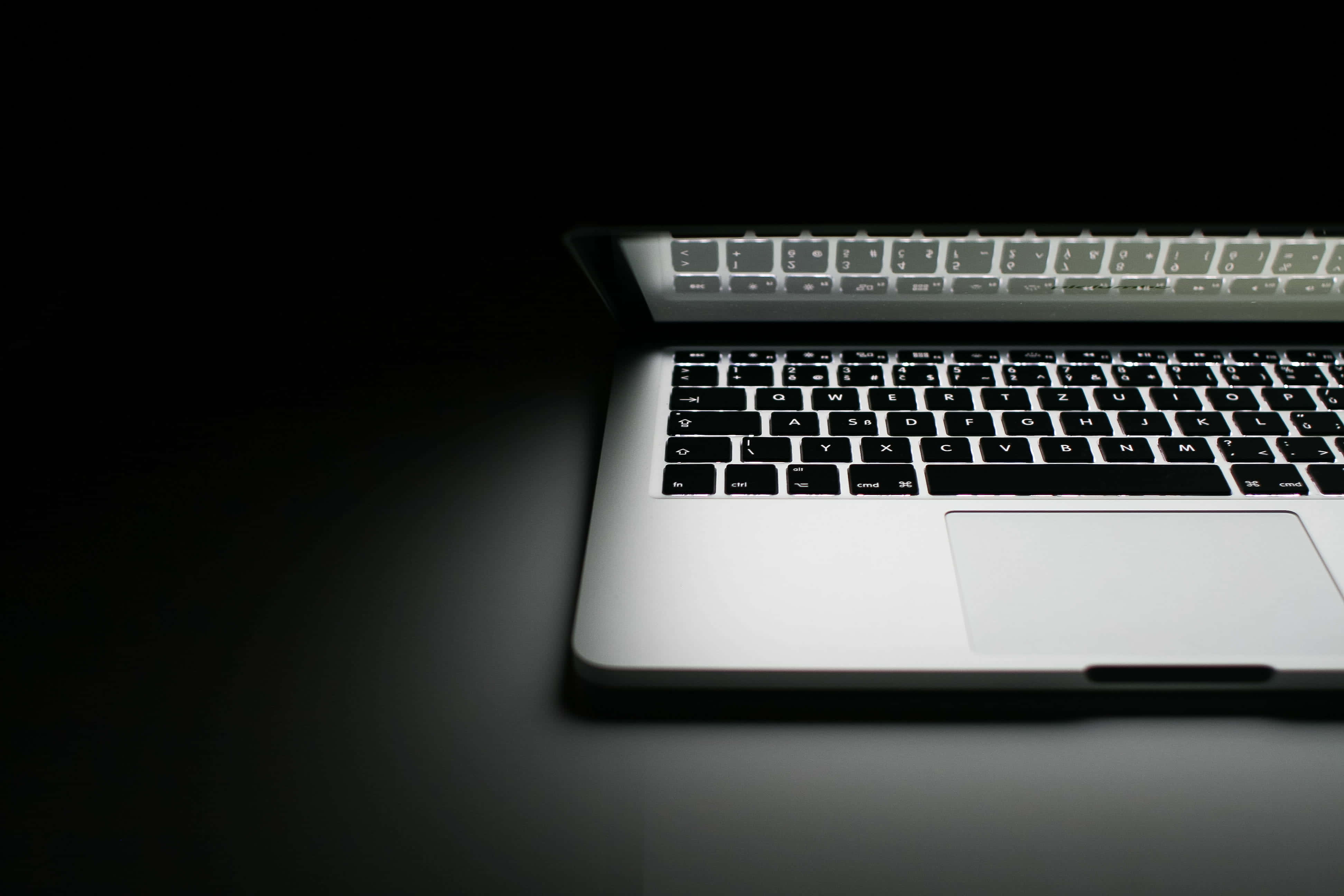 美學 MacBook 壁紙 桌布 壁紙 — 時尚的銀色筆記型電腦鍵盤在深黑色背景上柔和發光，帶有戲劇性的聚光燈效果。