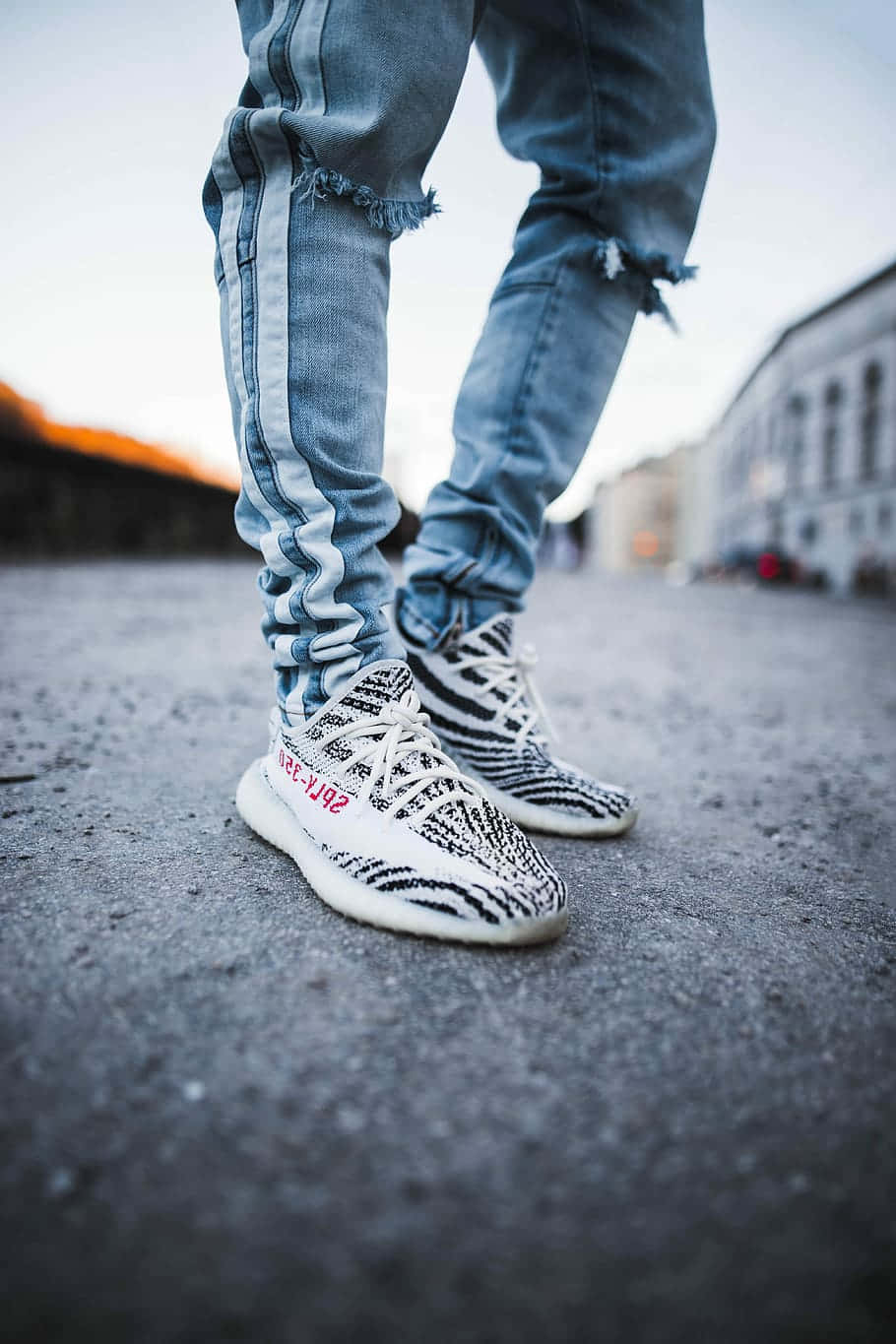 Sneaker 桌布 壁紙 — 時尚破洞牛仔褲與標誌性黑白運動鞋在黃金時段站立於城市人行道上的特寫。