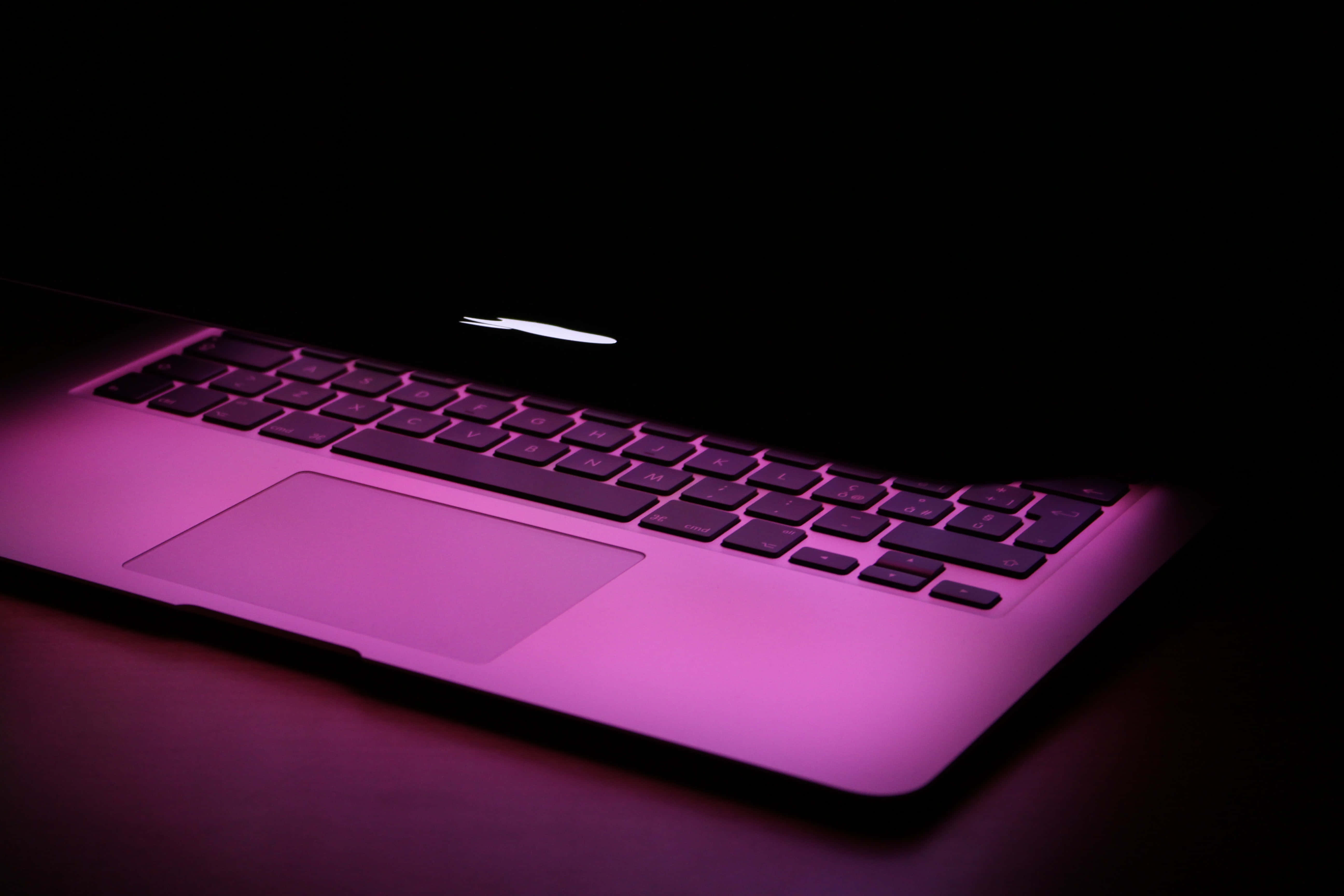美學 MacBook 壁紙 桌布 壁紙 — 時尚筆記型電腦鍵盤在深色背景下沐浴在充滿活力的紫色光中。