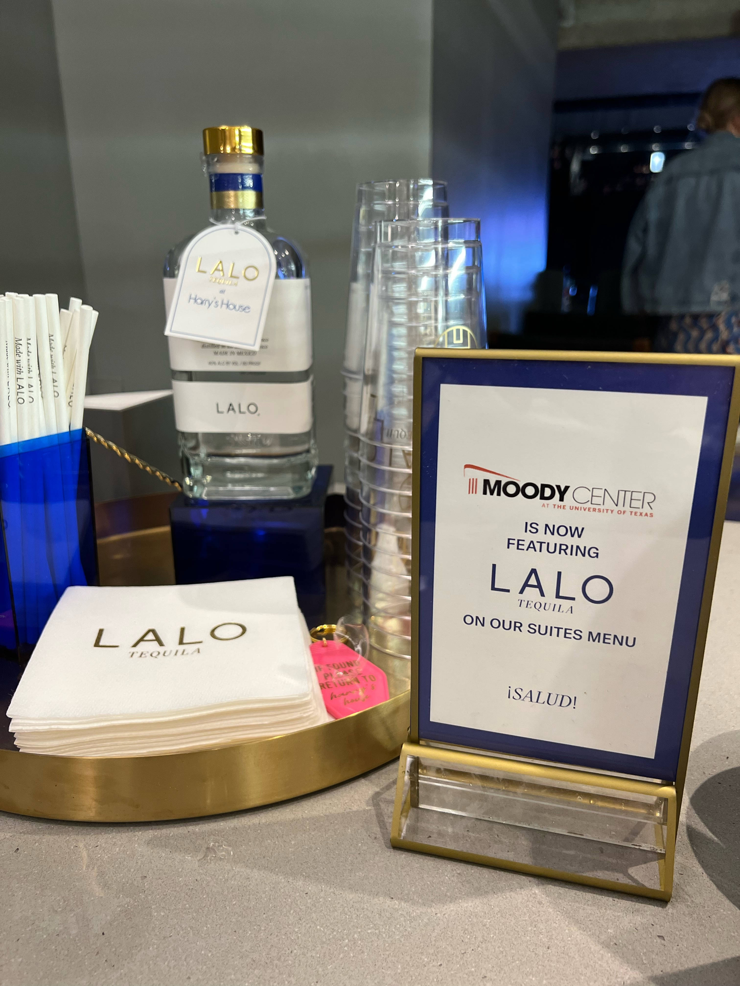 alcohol 桌布 壁紙 — 時尚酒吧設置，包括一瓶Lalo龍舌蘭酒、餐巾和一個標牌，宣佈其加入Moody Center套房的菜單。