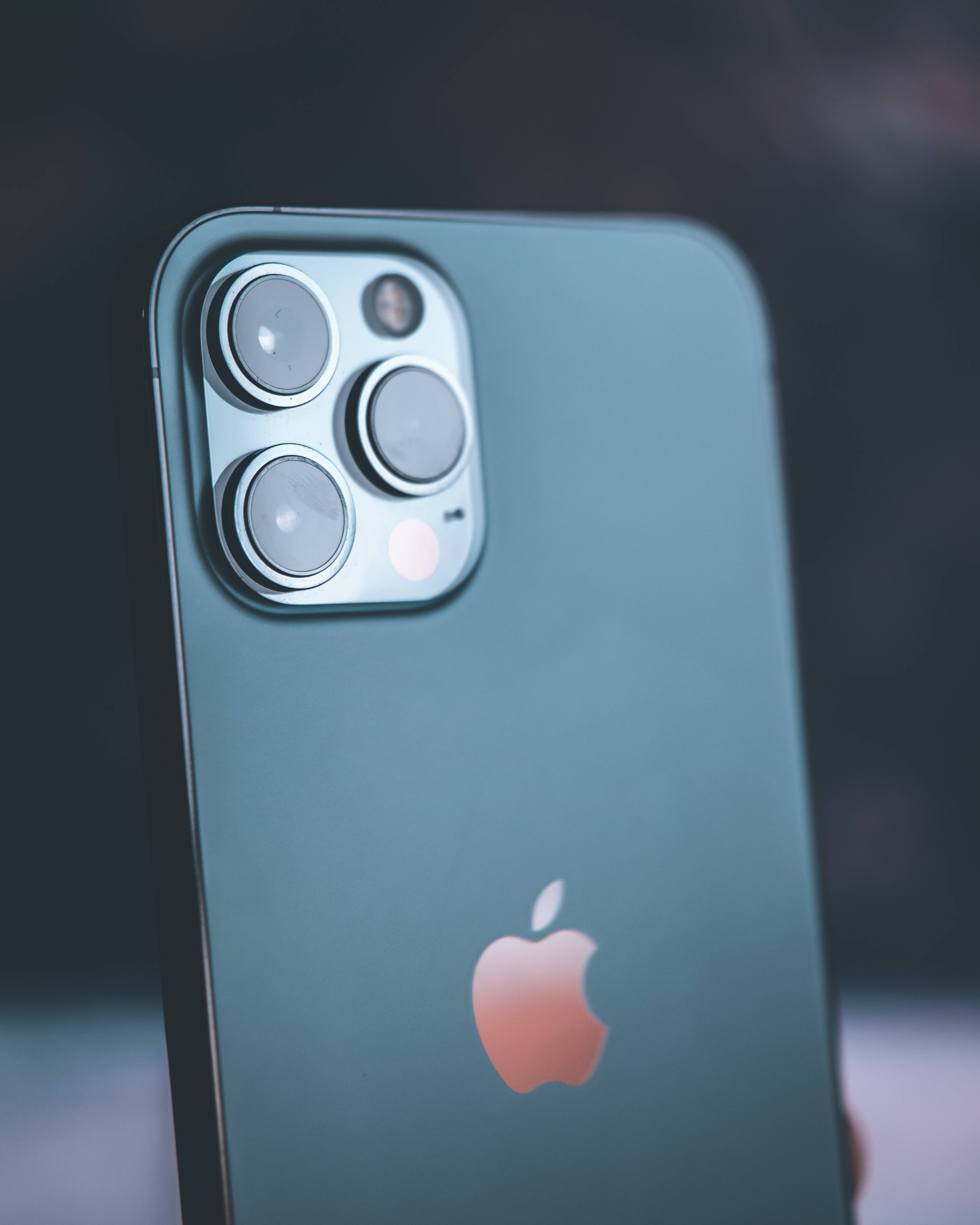 標誌 桌布 壁紙 — 時尚青綠色iPhone 14 Pro的特寫，具有其獨特的相機模組和發光的蘋果標誌，背景為模糊的深色。