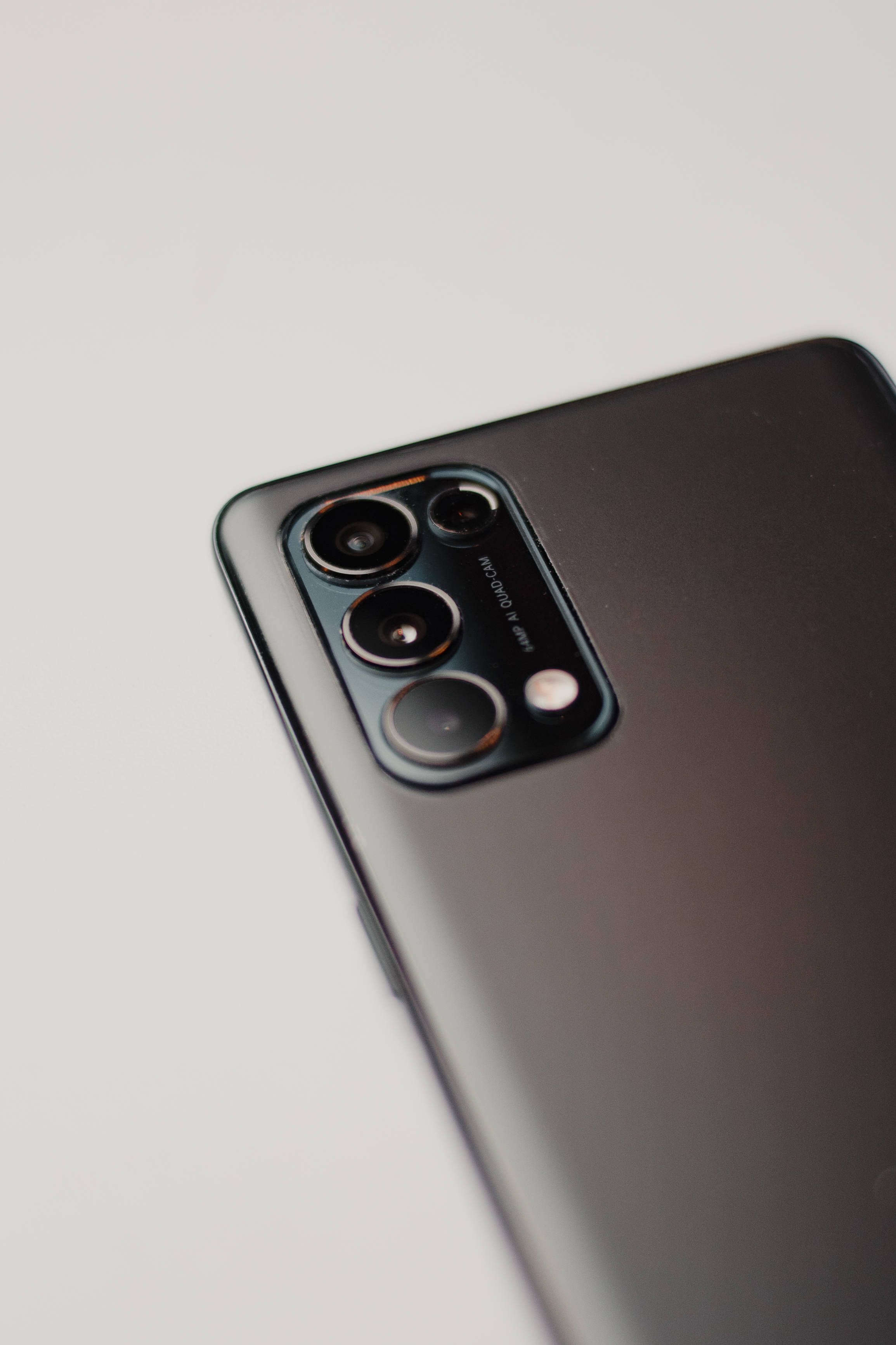 oppo 桌布 壁紙 — 時尚黑色智慧型手機相機模組的特寫，配備四個鏡頭和閃光燈，背景為簡約白色。