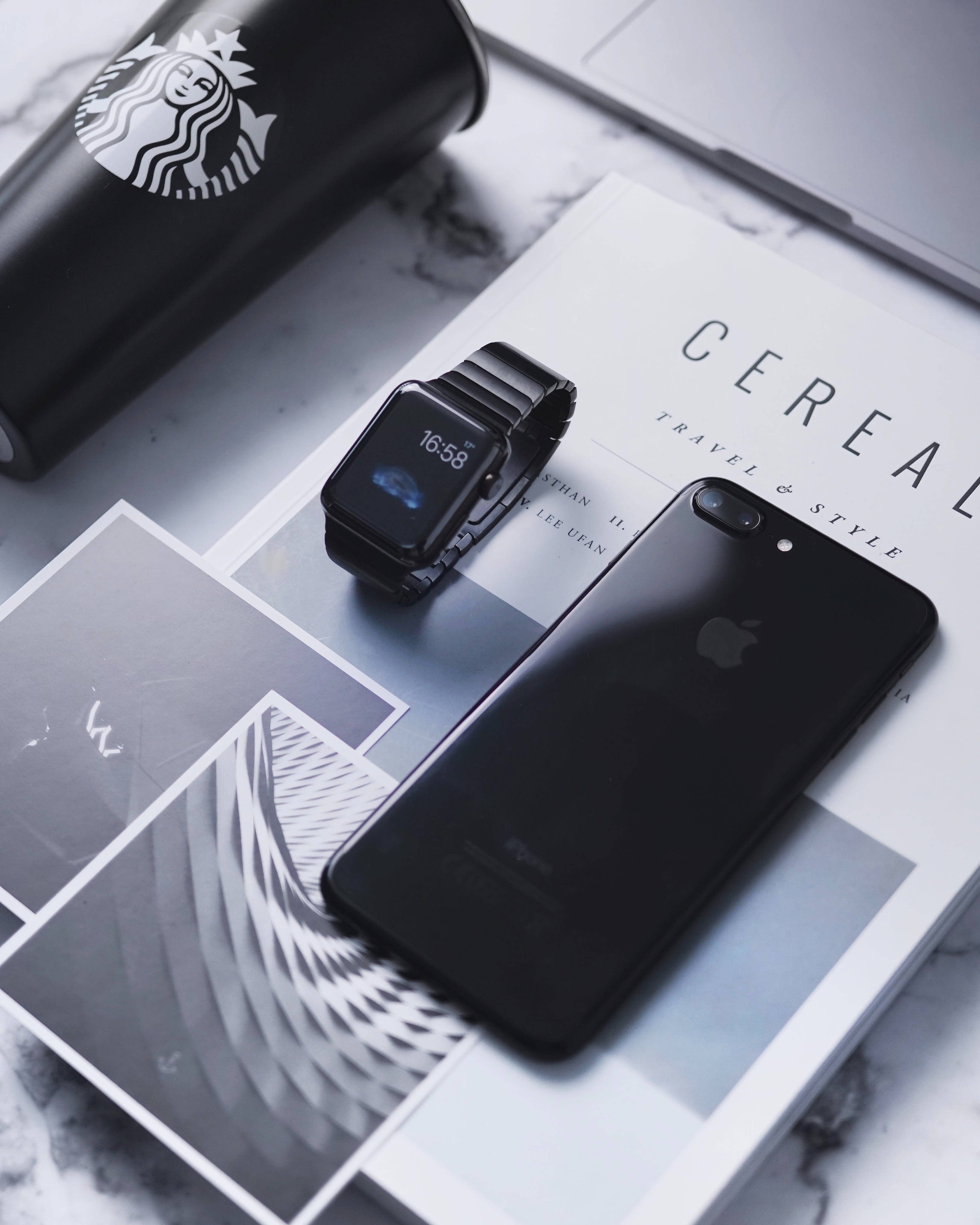 Apple Watch 動態 桌布 壁紙 — 時尚黑色智慧手錶和iPhone放在大理石表面的雜誌上，旁邊放著Starbucks杯。