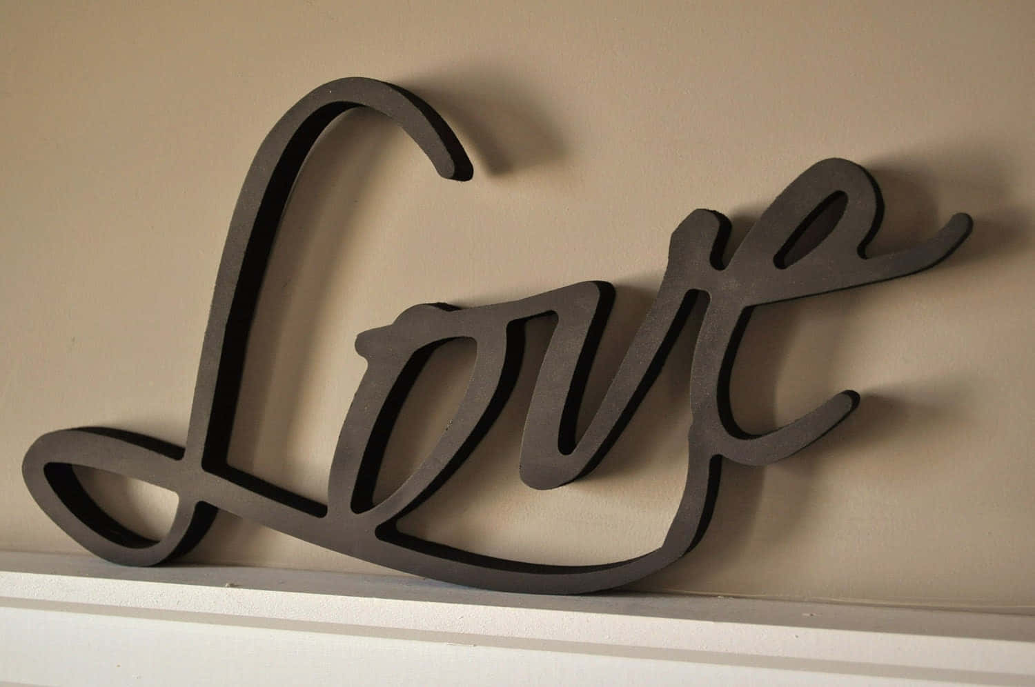 3d Love 桌布 壁紙 — 時尚黑色草書「Love」牆飾，在白色層架上方米色牆壁上投下柔和陰影。